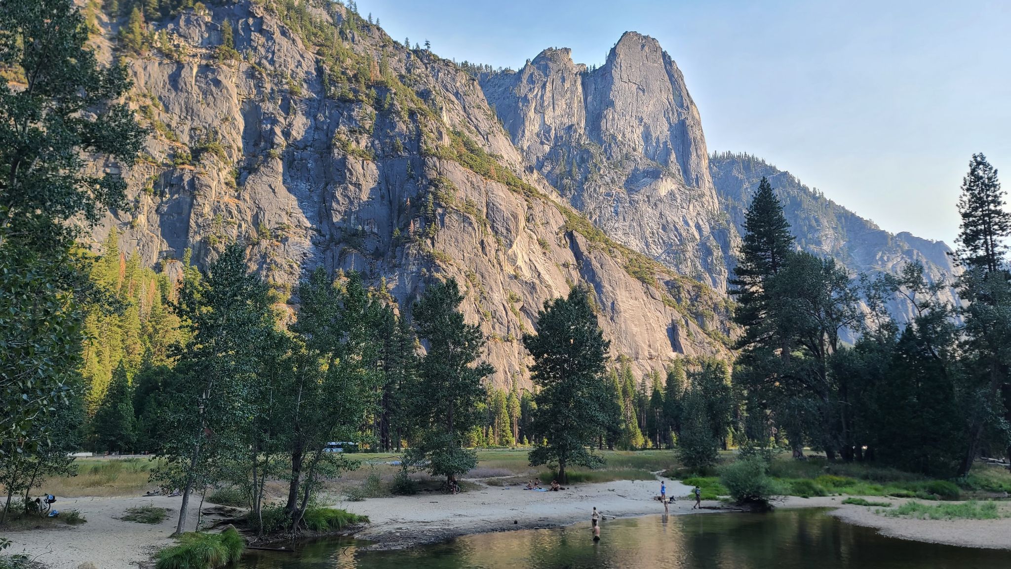 People wade in a river with sandy banks, surrounded by tall, sunlit mountains. - Swinging Bridge & Picnic Area – View of Yosemite Valley loop from Yosemite Valley