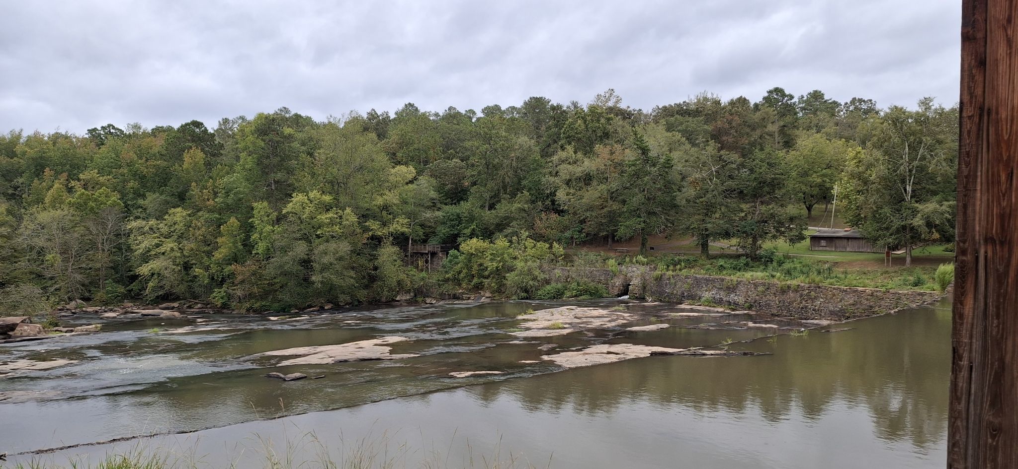 Overcast view of a wide river with exposed rocks and dense forest. - Watson Mill Covered Bridge loop from Winterville