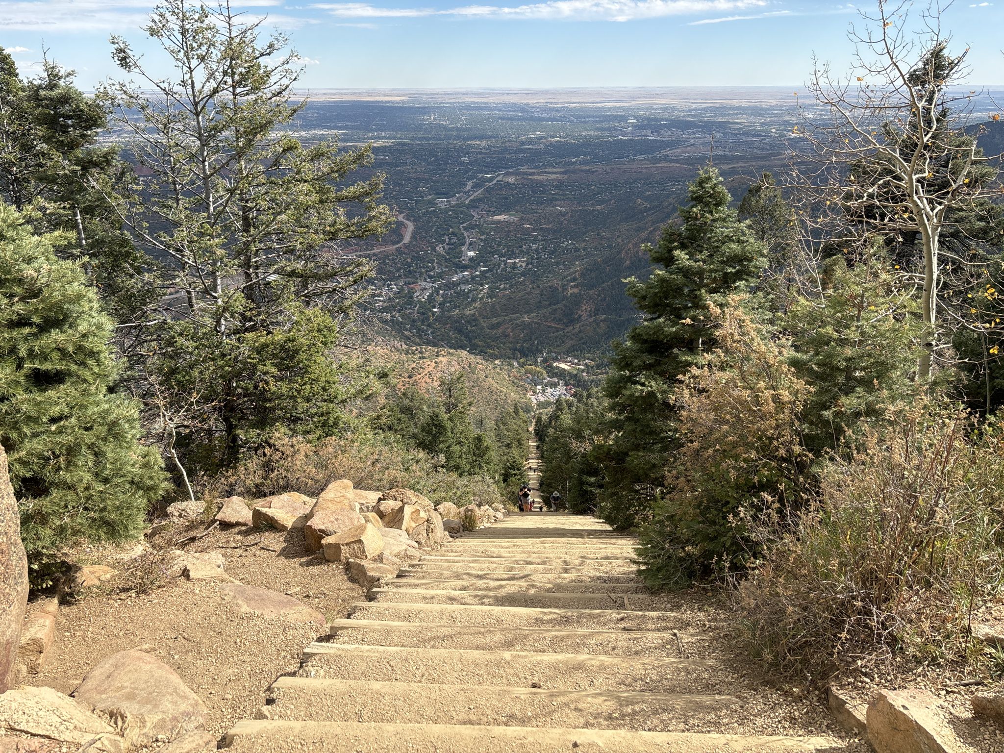 Steep stone stairs descend through a forest to a distant valley. - Manitou Incline and Barr Trail Loop