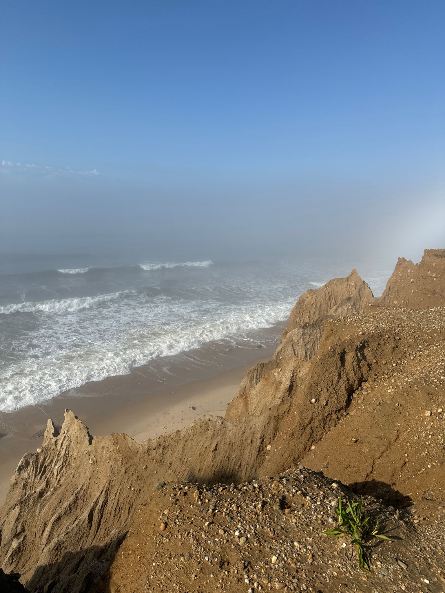 Ocean waves crash on a sandy beach below eroded cliffs on a misty day. - Rheinstein Estate Park loop from Shadmoor State Park
