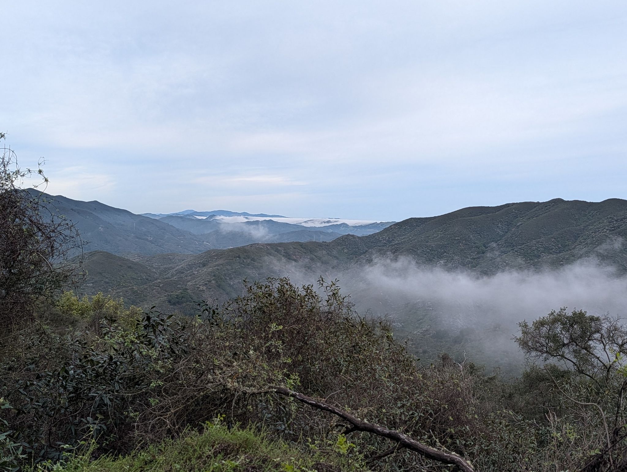 Overcast mountain landscape with fog settling in valleys and dense green foliage. - Cerro Alto Loop Trail