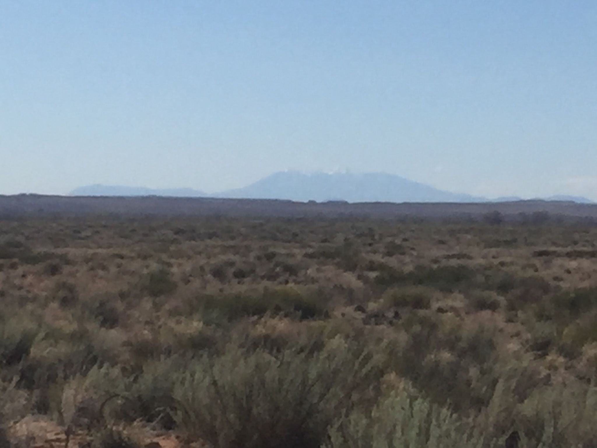 Vast arid landscape with scrub brush and distant snow-capped mountains under a clear sky. - Nusungvö, Diné, and Sunset Cemetery Loop