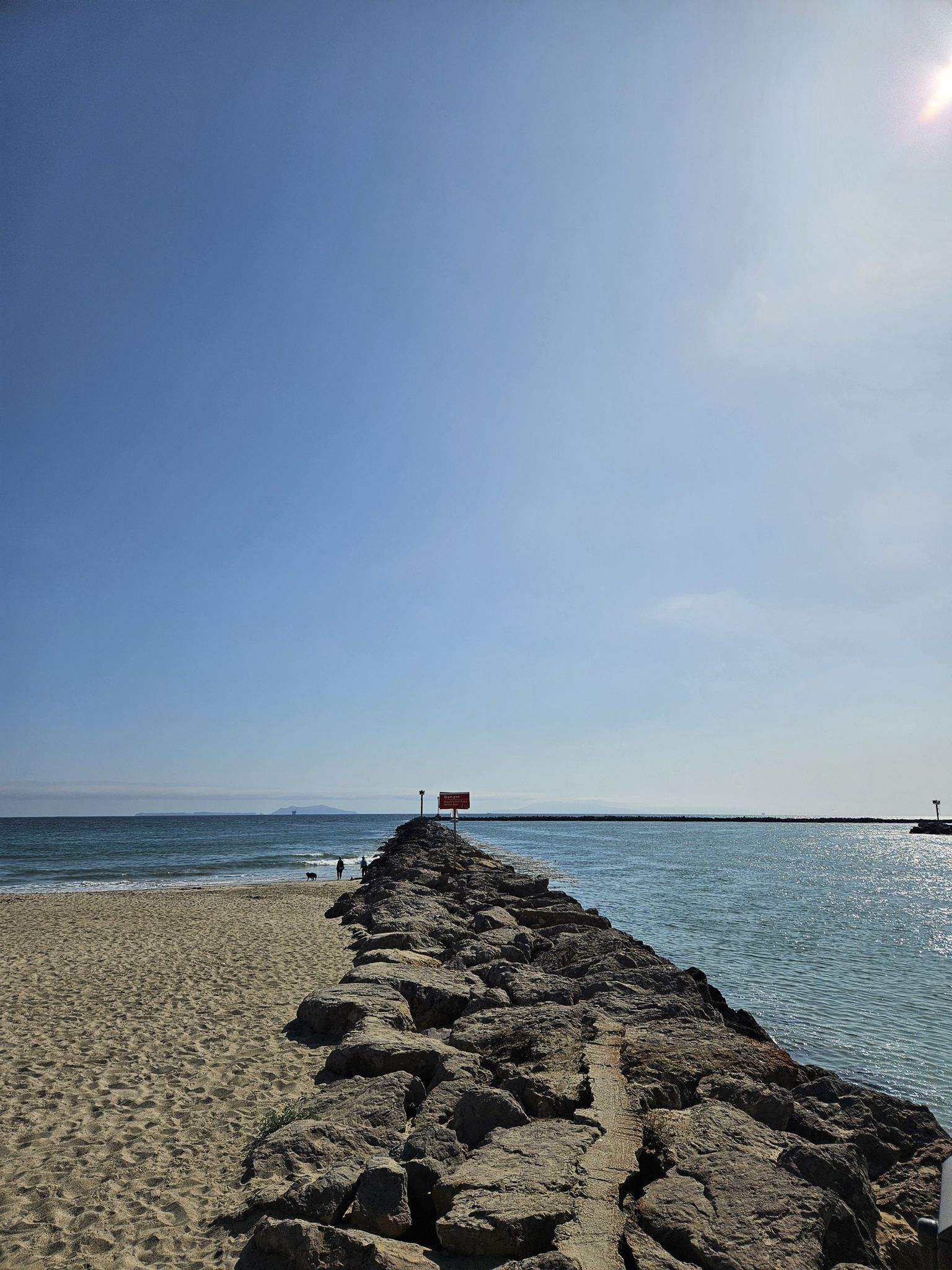Sunny day, rocky jetty extends into blue ocean from sandy beach. - Silver Strand Beach to La Jenelle Jetty Trail