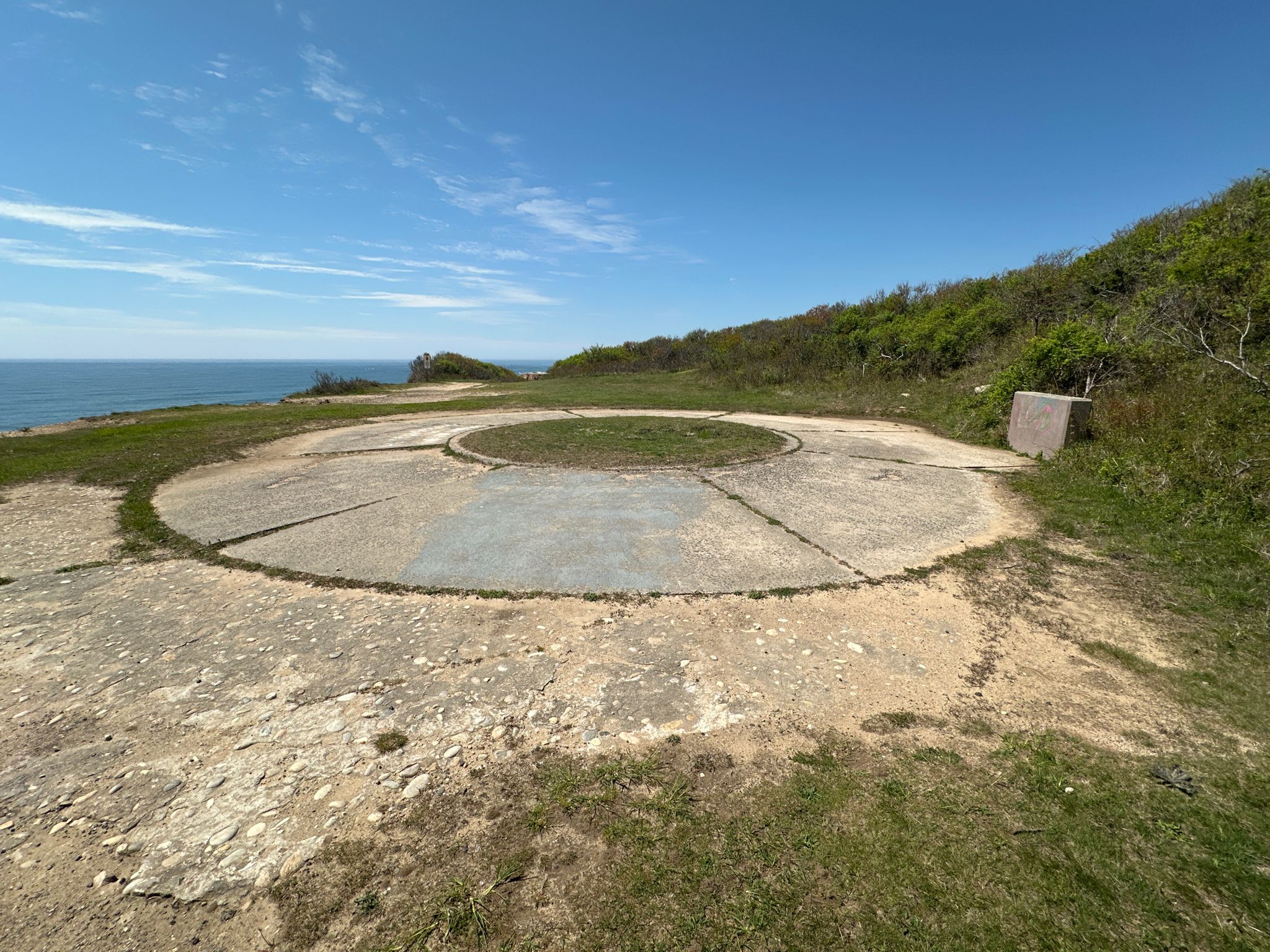 Circular concrete pad on a grassy clifftop overlooking the ocean under a clear sky. - Paumanok Path: Montauk Point Loop