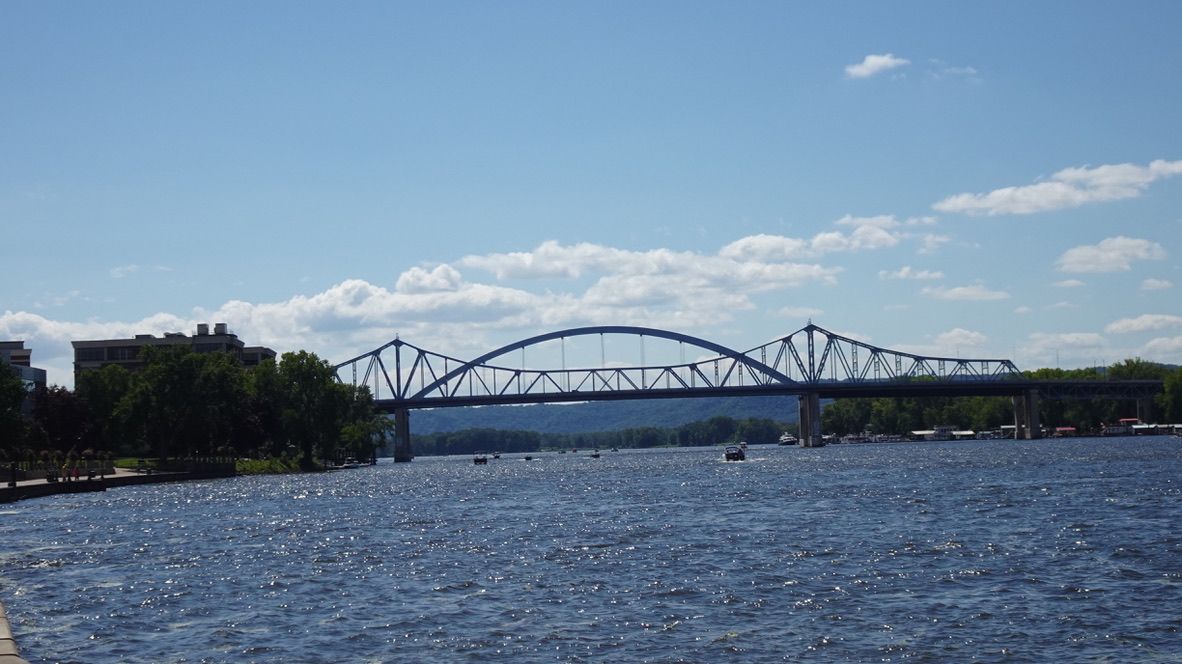 Large blue truss bridge over a sunny river with boats, under a bright sky. - Riverside Park loop from University of Wisconsin-La Crosse