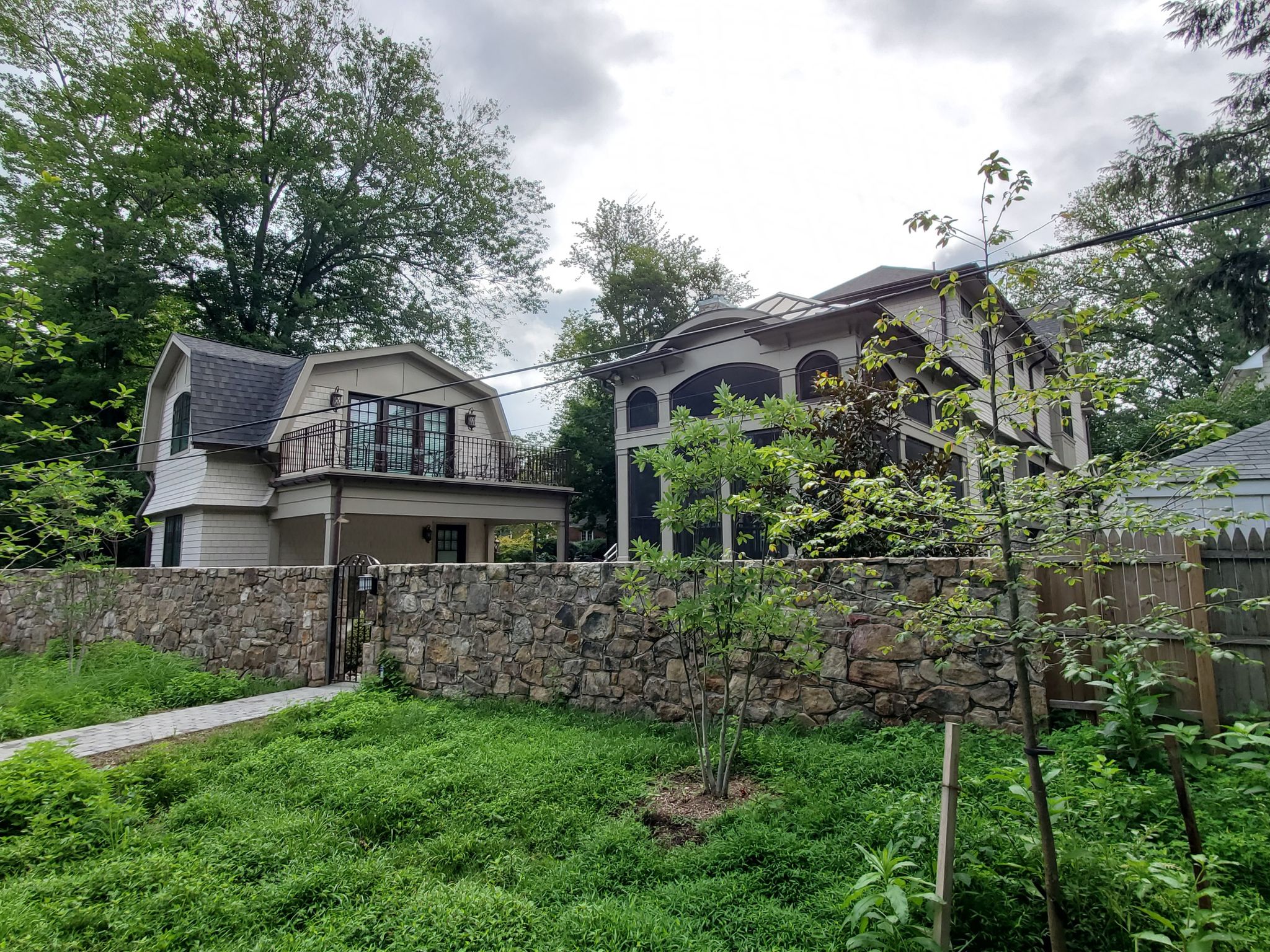 Two houses behind a stone wall, surrounded by green trees and grass. - Capital Crescent Trail loop from Brookmont