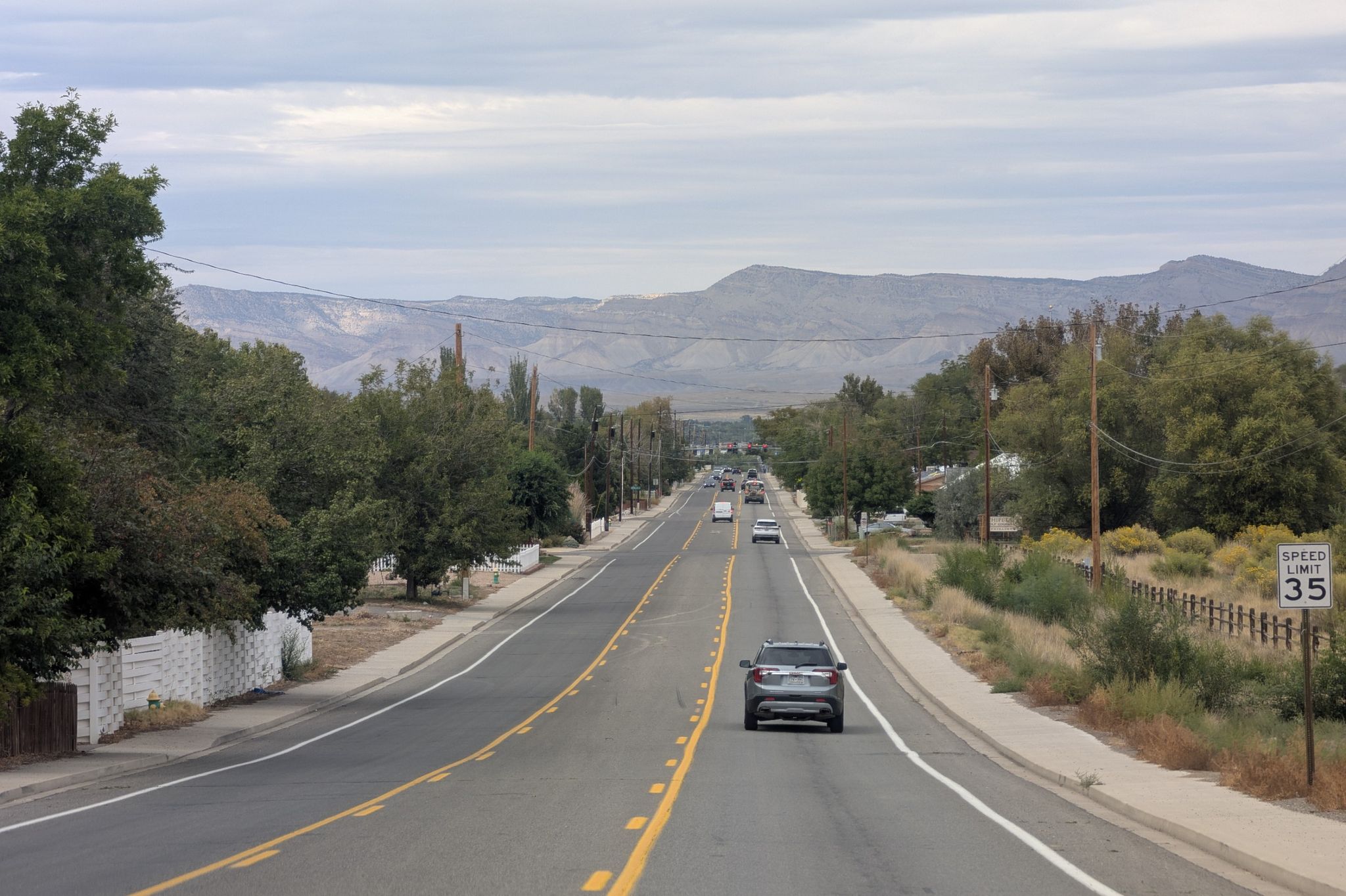 A multi-lane highway with cars driving towards distant mountains under an overcast sky. - Fruit and Wine Byway - East Orchard Mesa Loop