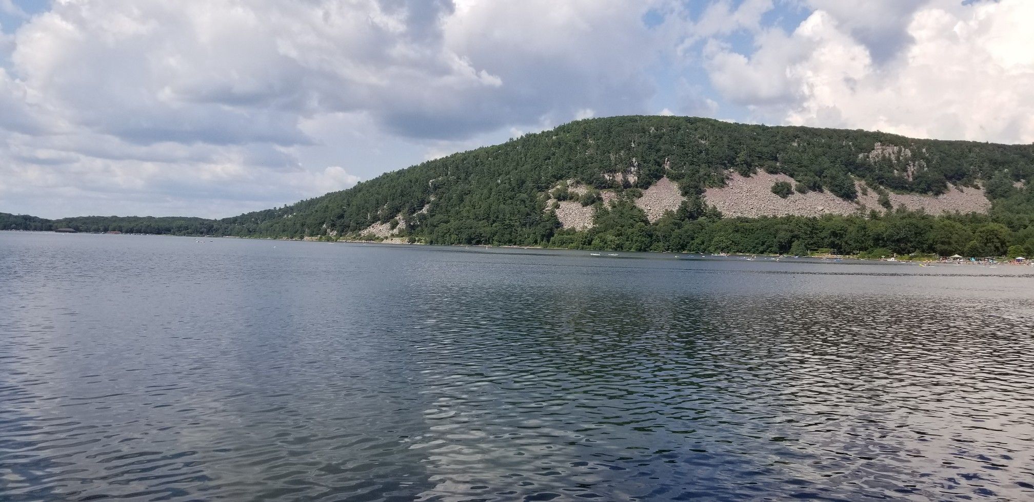 Wide view of a lake with forested hills and rocky slopes under clouds. - Ringling Bungalow Foundation loop from Devil's Lake State Park