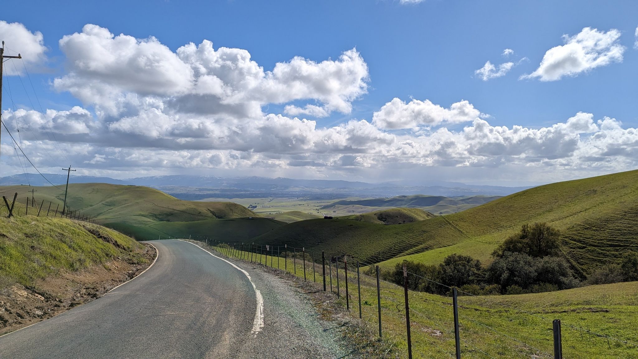 Paved road winding through green hills under a partly cloudy blue sky. - Morgan Territory Road Loop