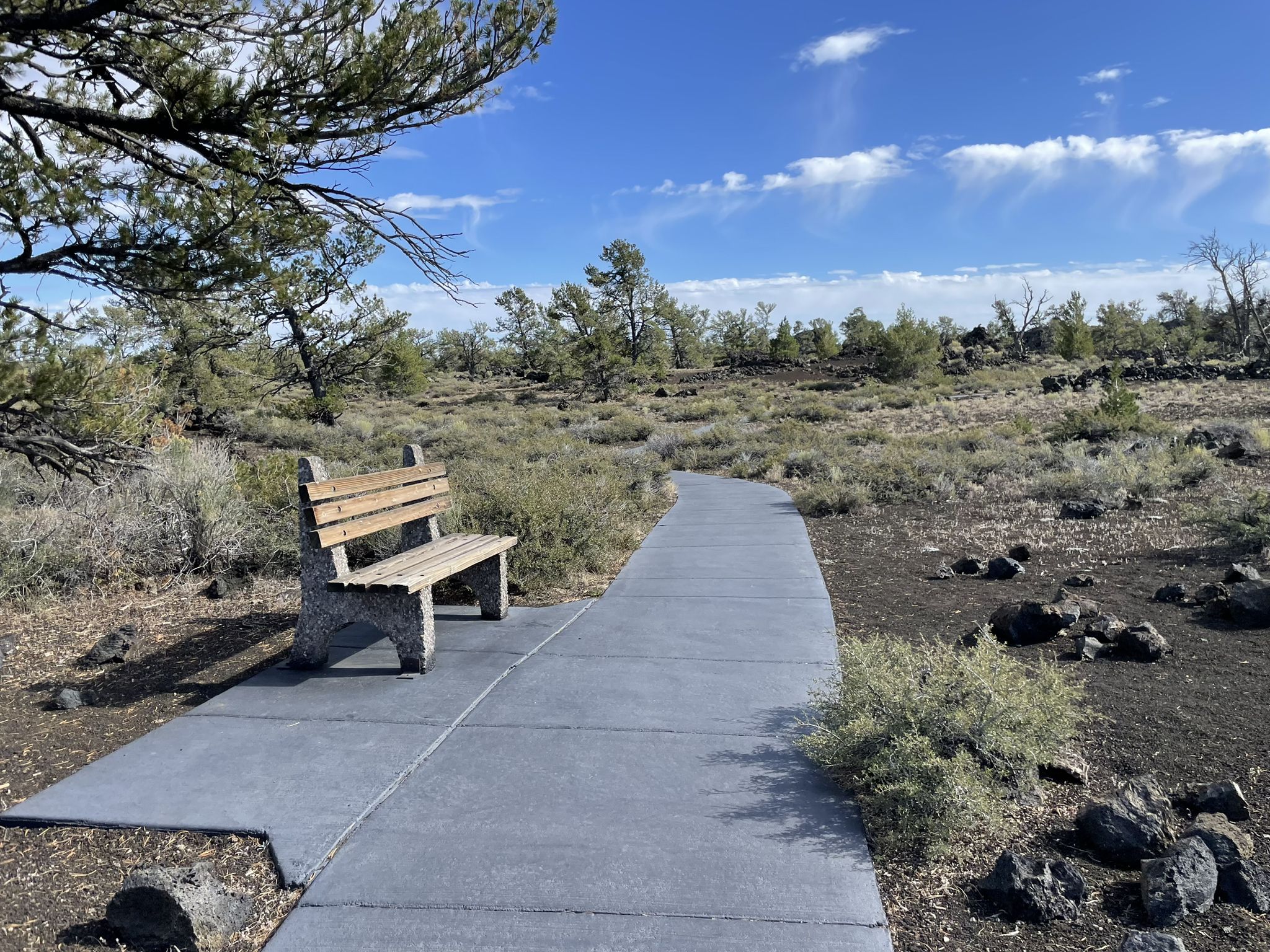 A wooden bench sits beside a paved path in a rocky, arid landscape. - Devils Orchard Nature Trail
