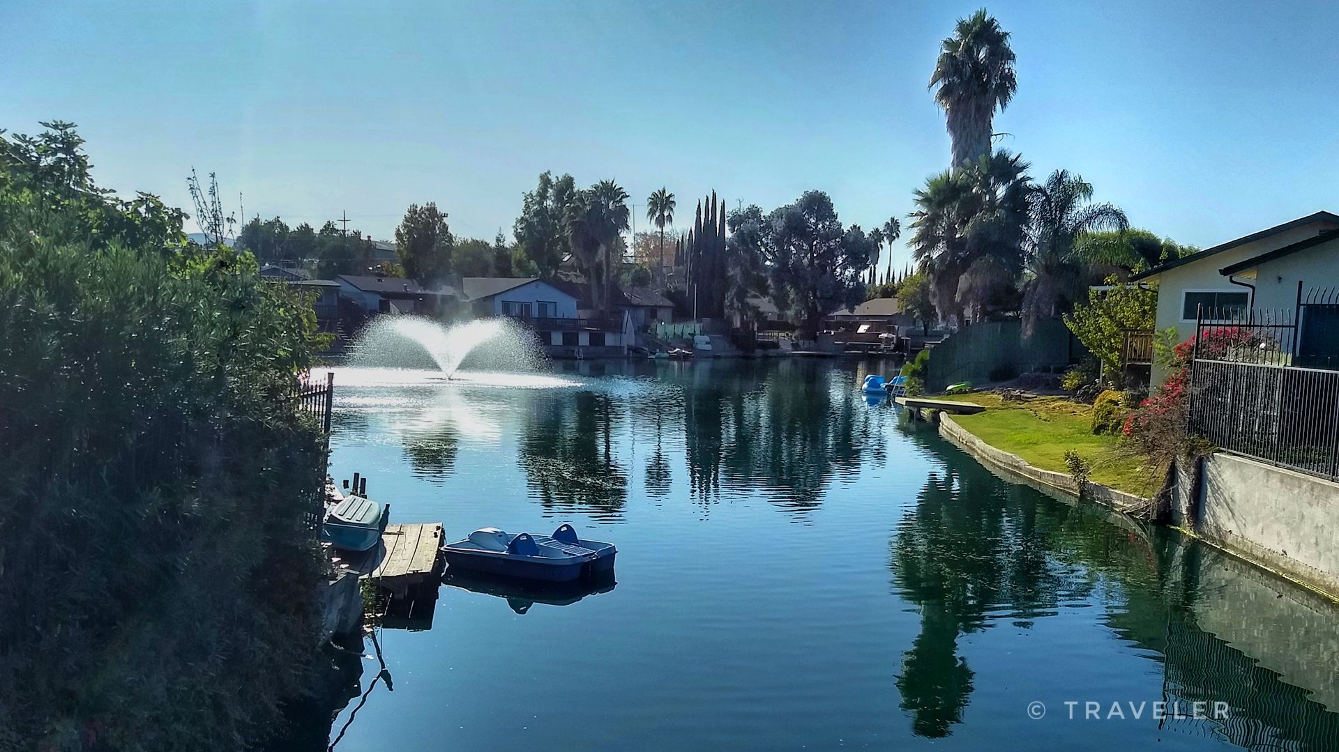 Sunny canal with fountain, houses, and small boats reflecting on calm water. - Lake Alhambra/Byron loop