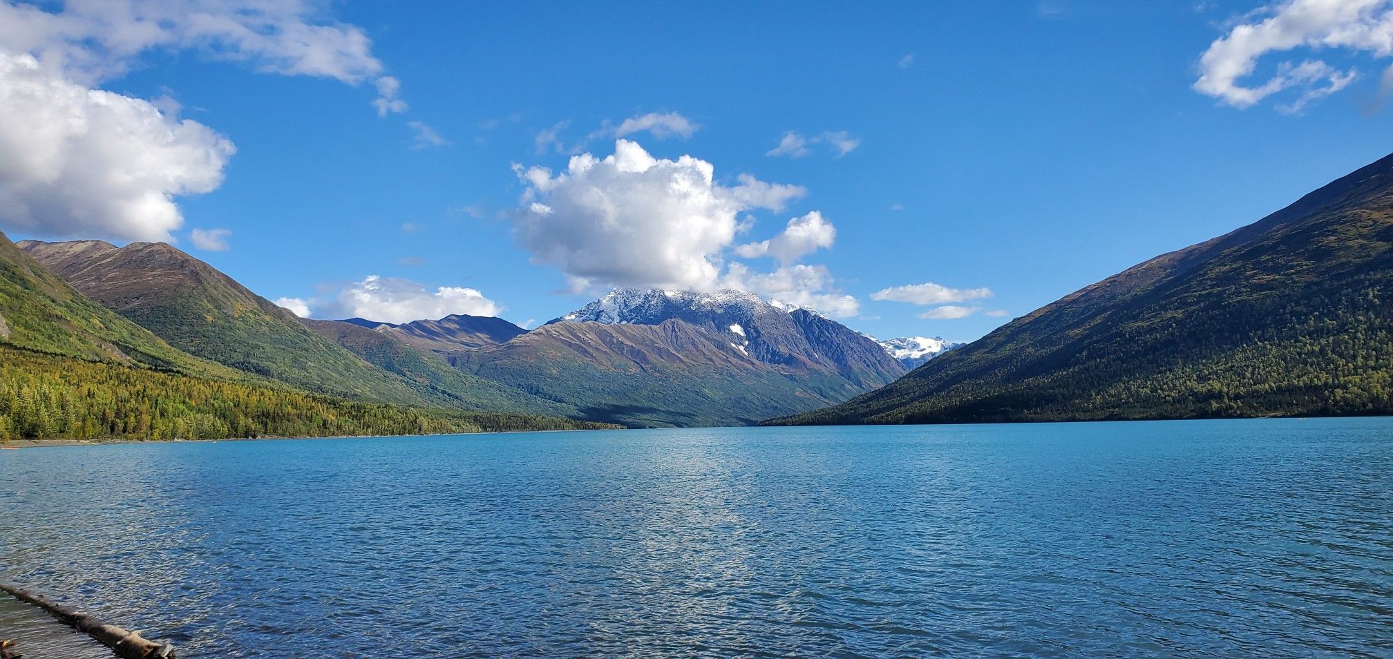 Bright blue lake surrounded by green mountains under a sunny, cloudy sky. - Eydlu Bena Loop Trail