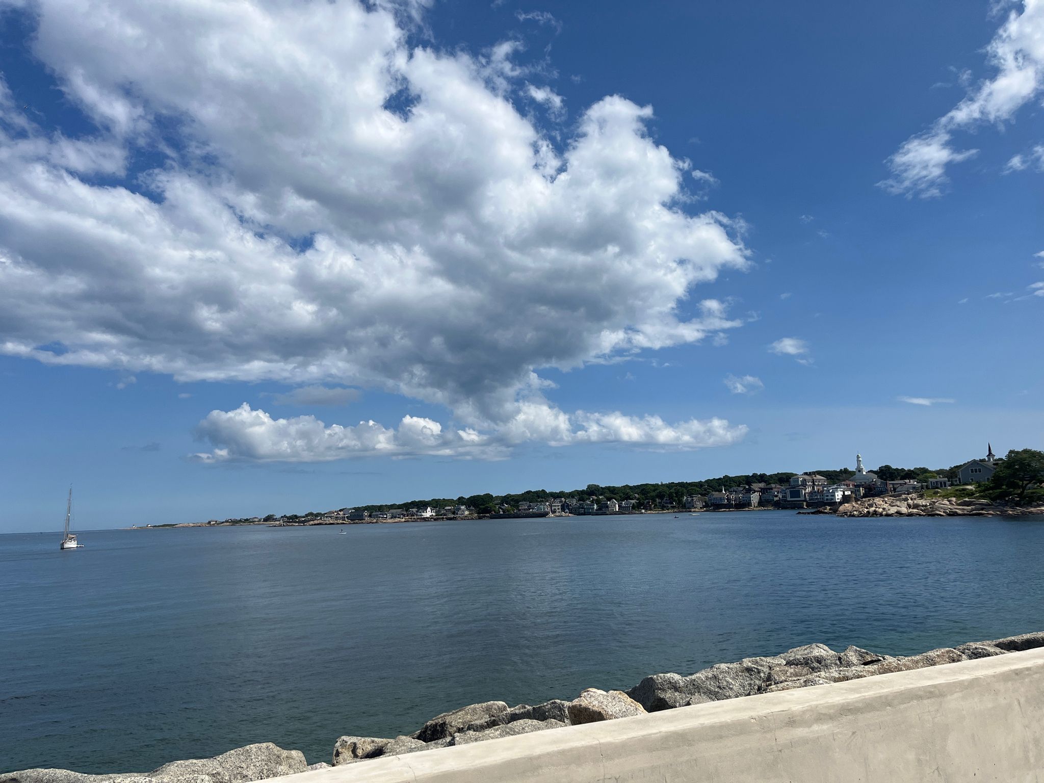 Calm ocean view with a distant town under a bright, cloudy sky. - Back Beach – Barred Owl Trail loop from Rockport
