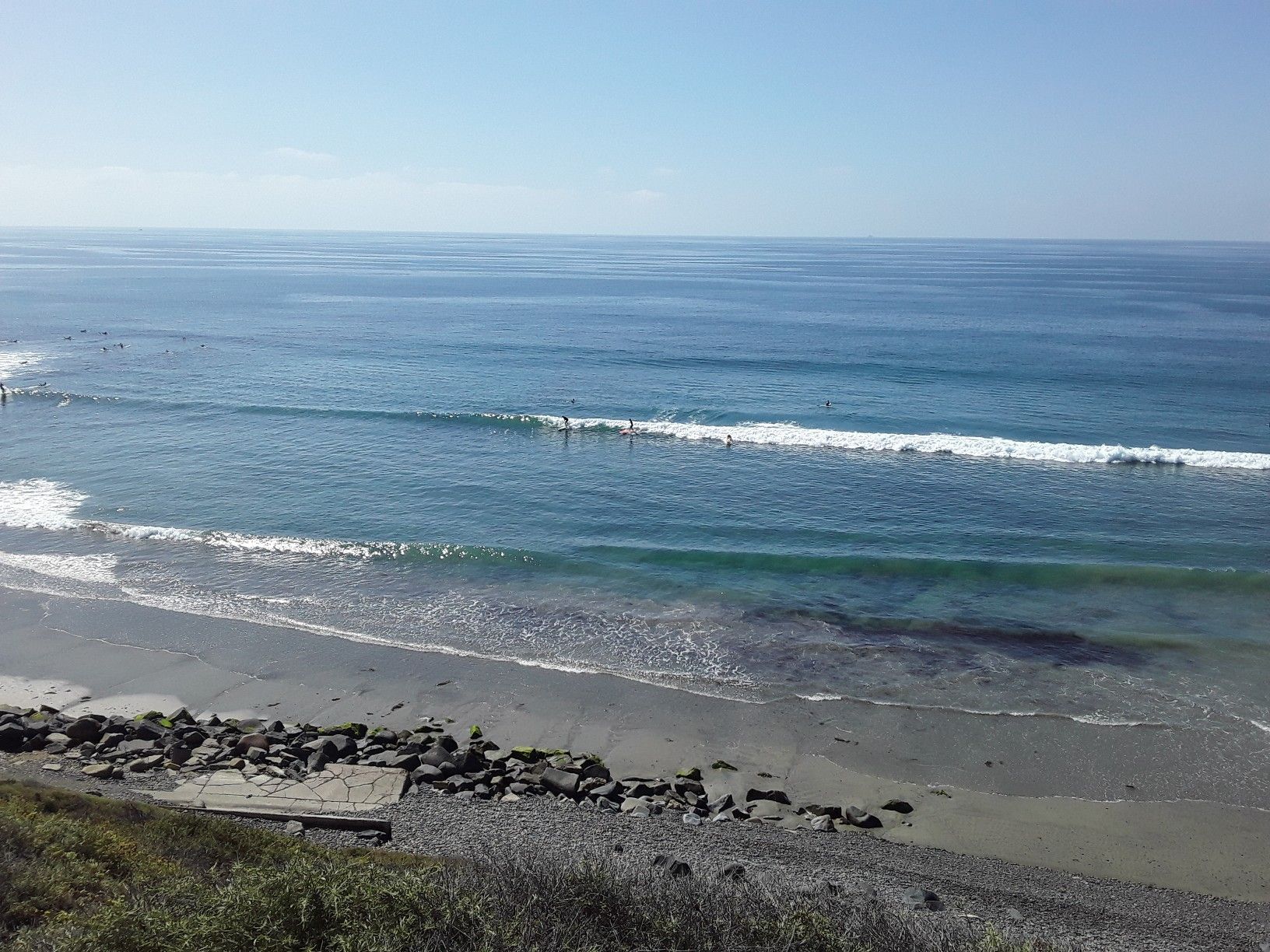 Wide ocean view with surfers in waves and a rocky beach under a clear sky. - Cardiff State Beach – San Elijo Lagoon Estuary Canal loop from Solana Beach