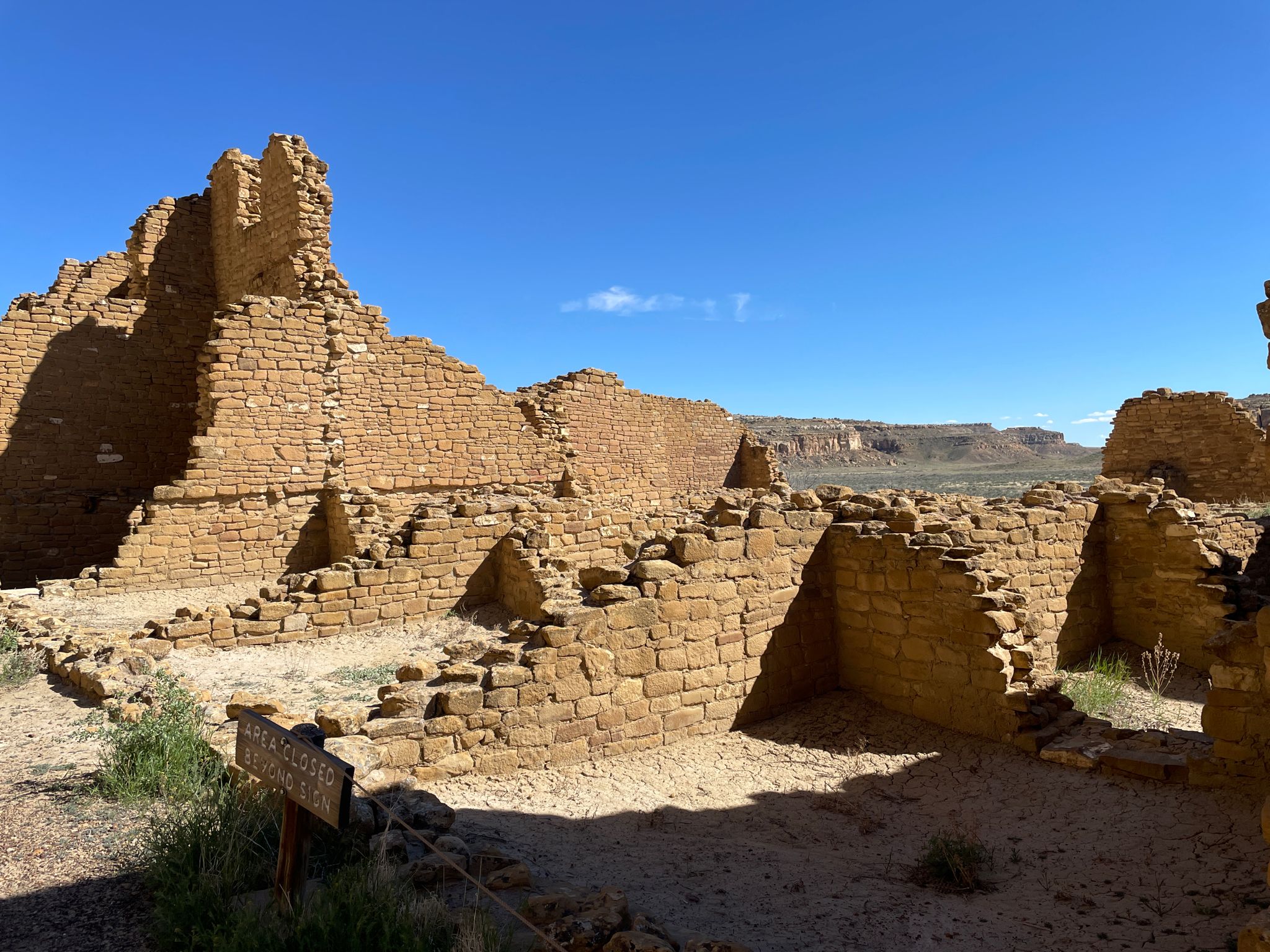 Expansive ancient stone ruins with walls and rooms under a bright blue sky. - Kin Kletso Trail