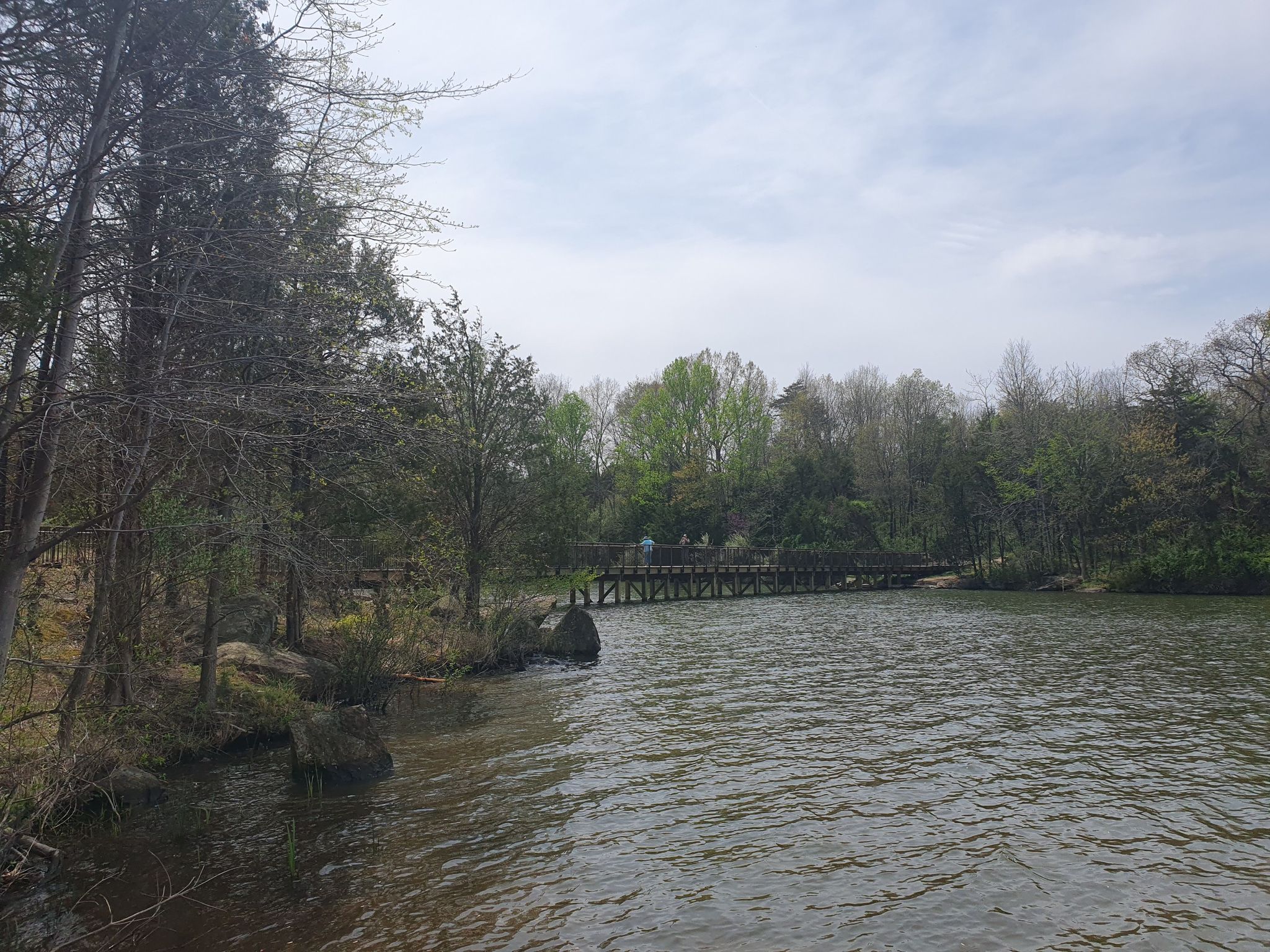 Wooden bridge over a lake, surrounded by trees under a cloudy sky. - Beaverdam Reservoir Trail