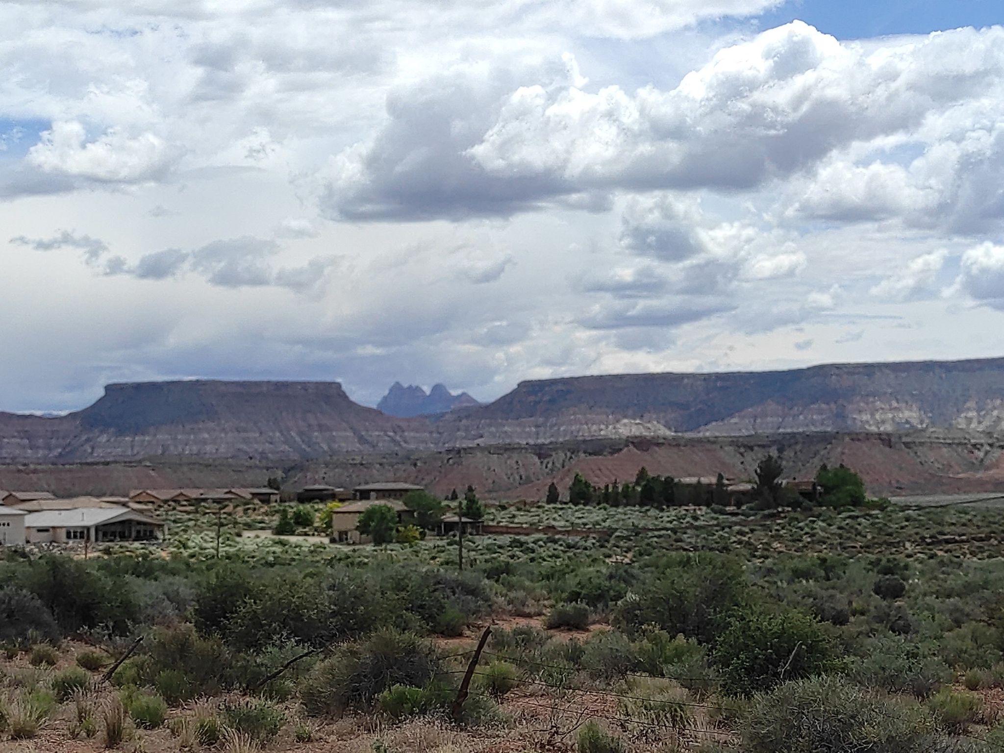 Desert landscape with distant mesas, scrub brush, and scattered houses under cloudy sky. - Hurricane, Utah to Lava Point Road