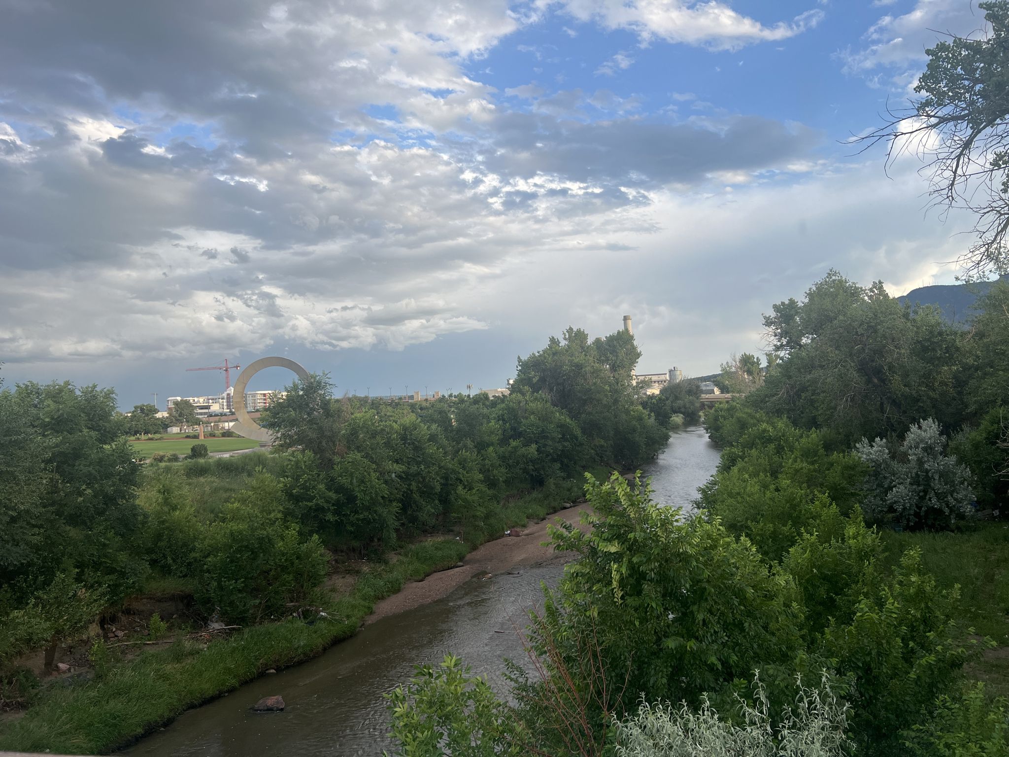 River winding through green trees with distant urban elements under cloudy sky. - Uintah street bridge – Pikes Peak Greenway loop from Colorado Springs
