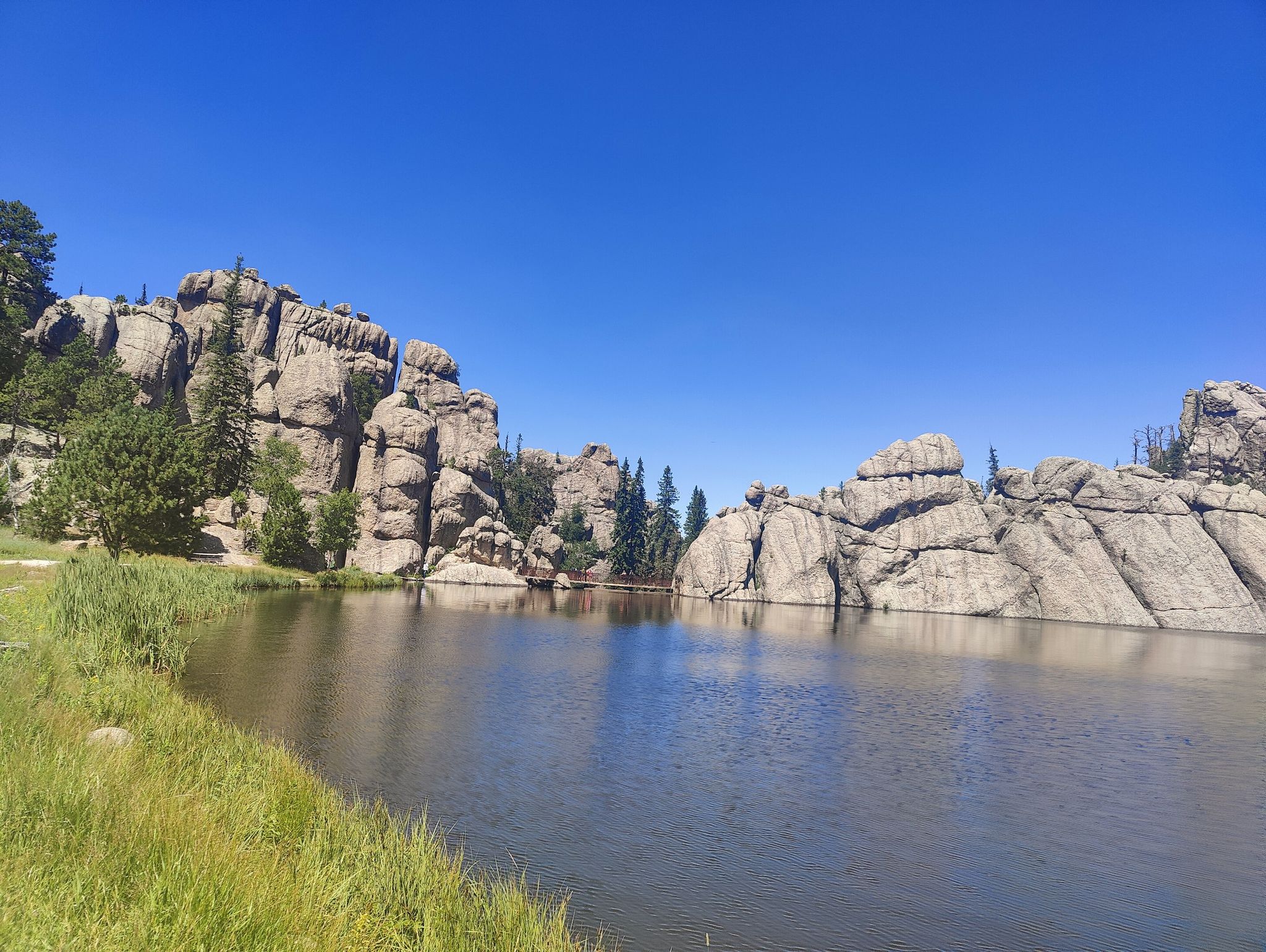A serene lake surrounded by large, weathered rock formations under a clear sky. - Sylvan Lake – Stockade Lake loop from Poppy Lode Mine