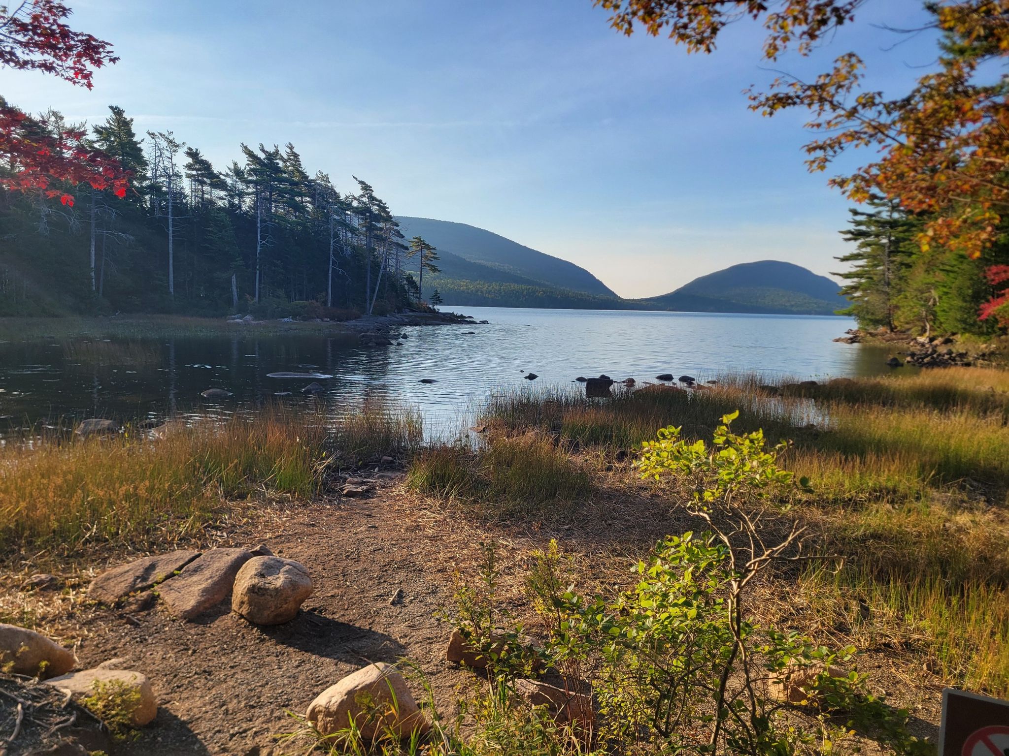 A calm lake with distant mountains and a grassy, tree-lined shore. - Eagle Lake – Eagle Lake — North Parking Lot loop from Ox Hill