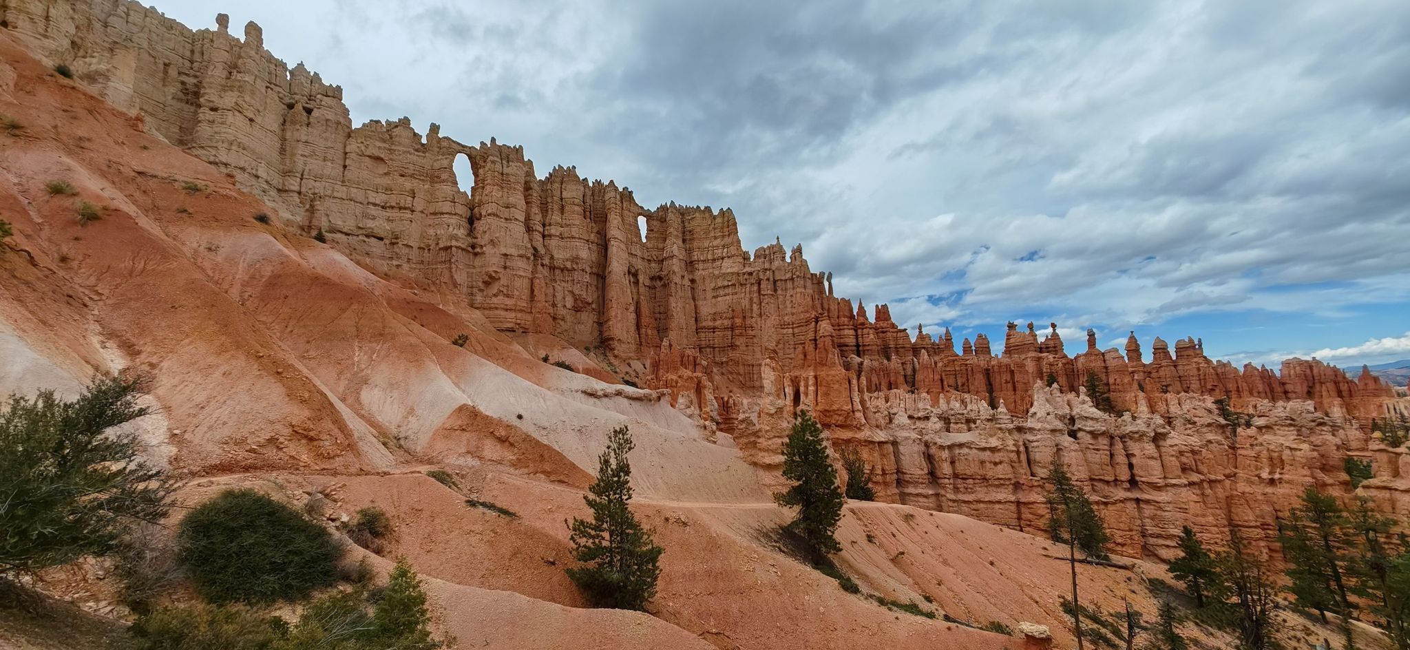 Red rock formations with a natural arch under a cloudy sky. - Red Canyon Arch – Lower Inspiration Point loop from Black Mountain