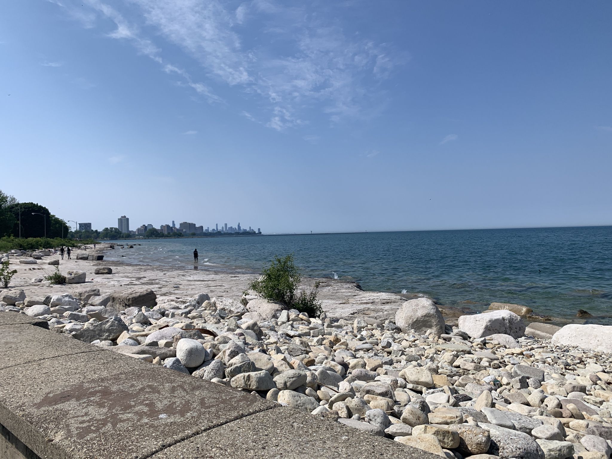 Rocky beach and blue water, with a distant city skyline under clear sky. - Lakefront Trail