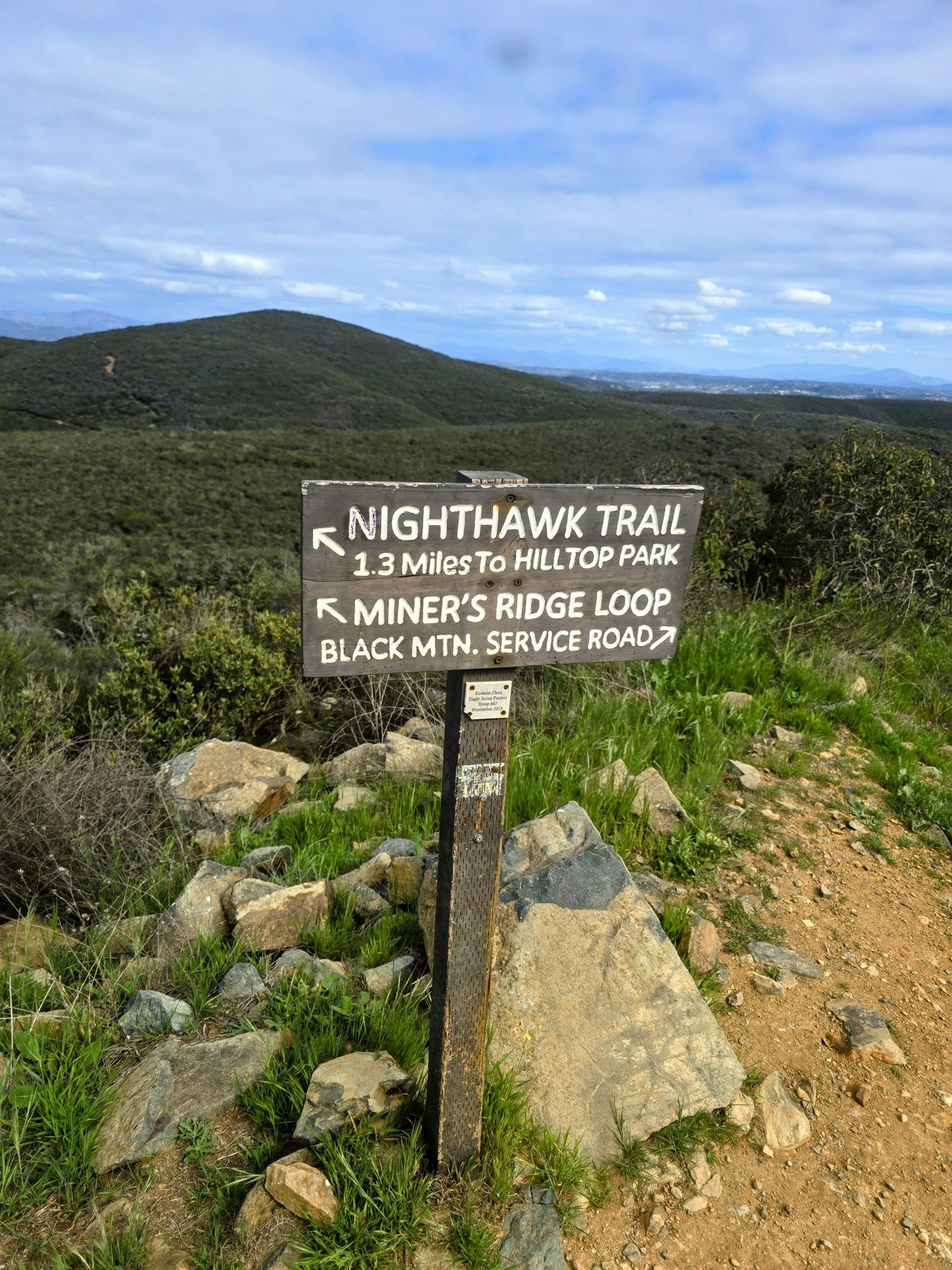 Wooden trail sign on a dirt path with distant green hills under a cloudy sky. - Black Mountain loop from Rancho Peñasquitos
