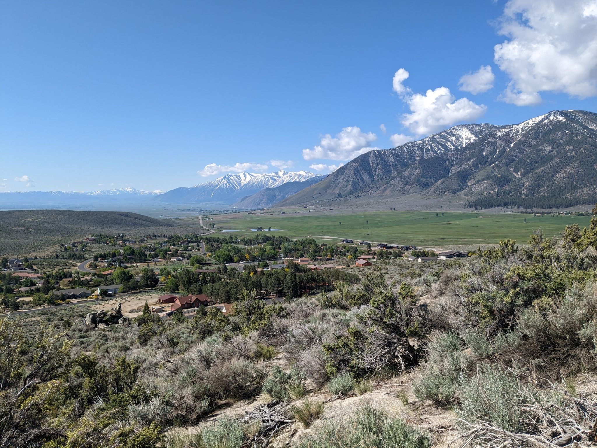 Panoramic view of a valley with a town, green fields, and snow-capped mountains. - Genoa – Nevada State Railroad Museum loop from Carson & Mills Park Railroad