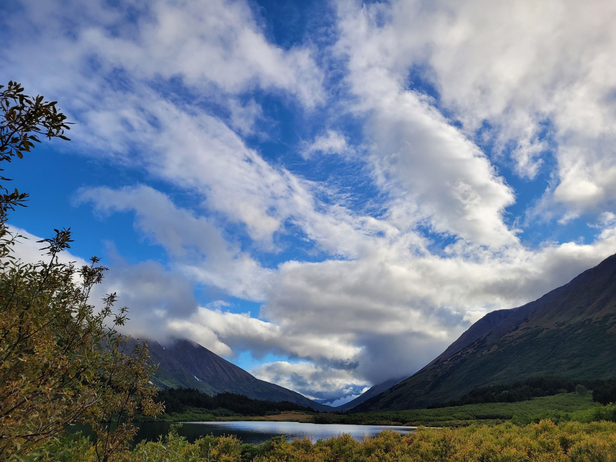 A serene lake nestled in a mountain valley under a bright, cloudy sky. - Carter Lake Trail