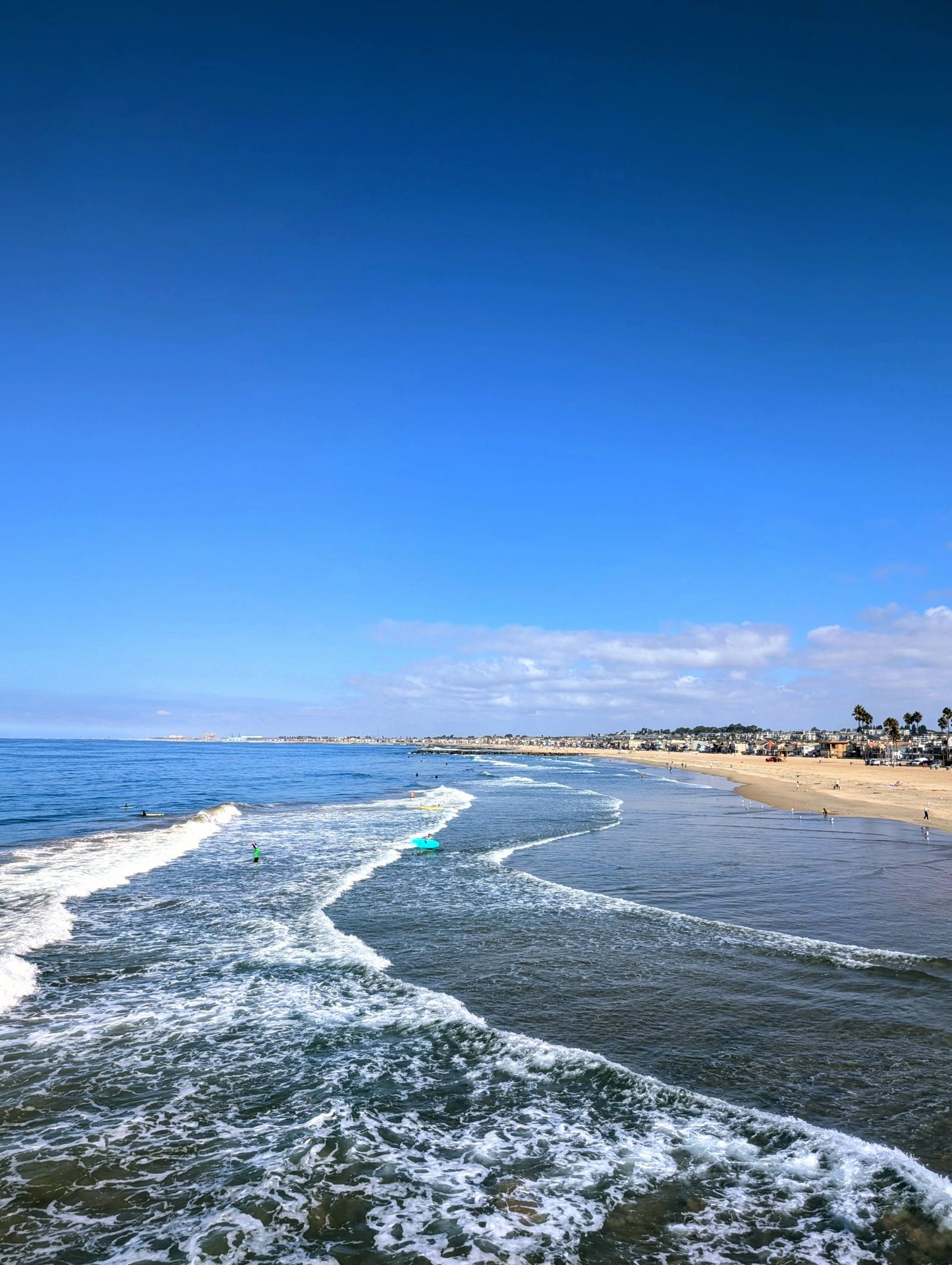 Ocean waves rolling onto a sandy beach under a clear blue sky. - Newport Pier to Balboa Pier