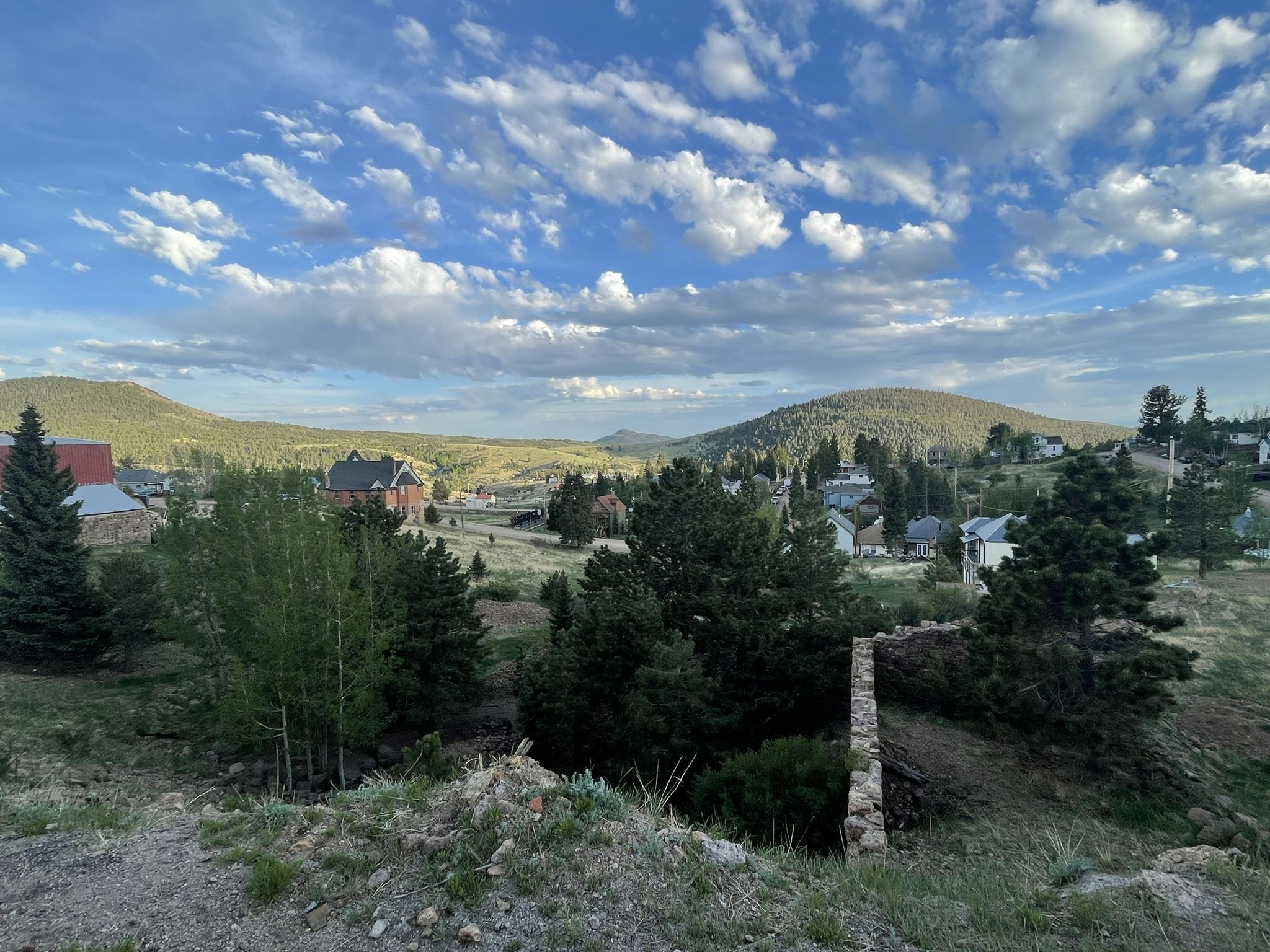 A small town in a valley surrounded by green hills under a cloudy sky. - Victor loop from Cripple Creek