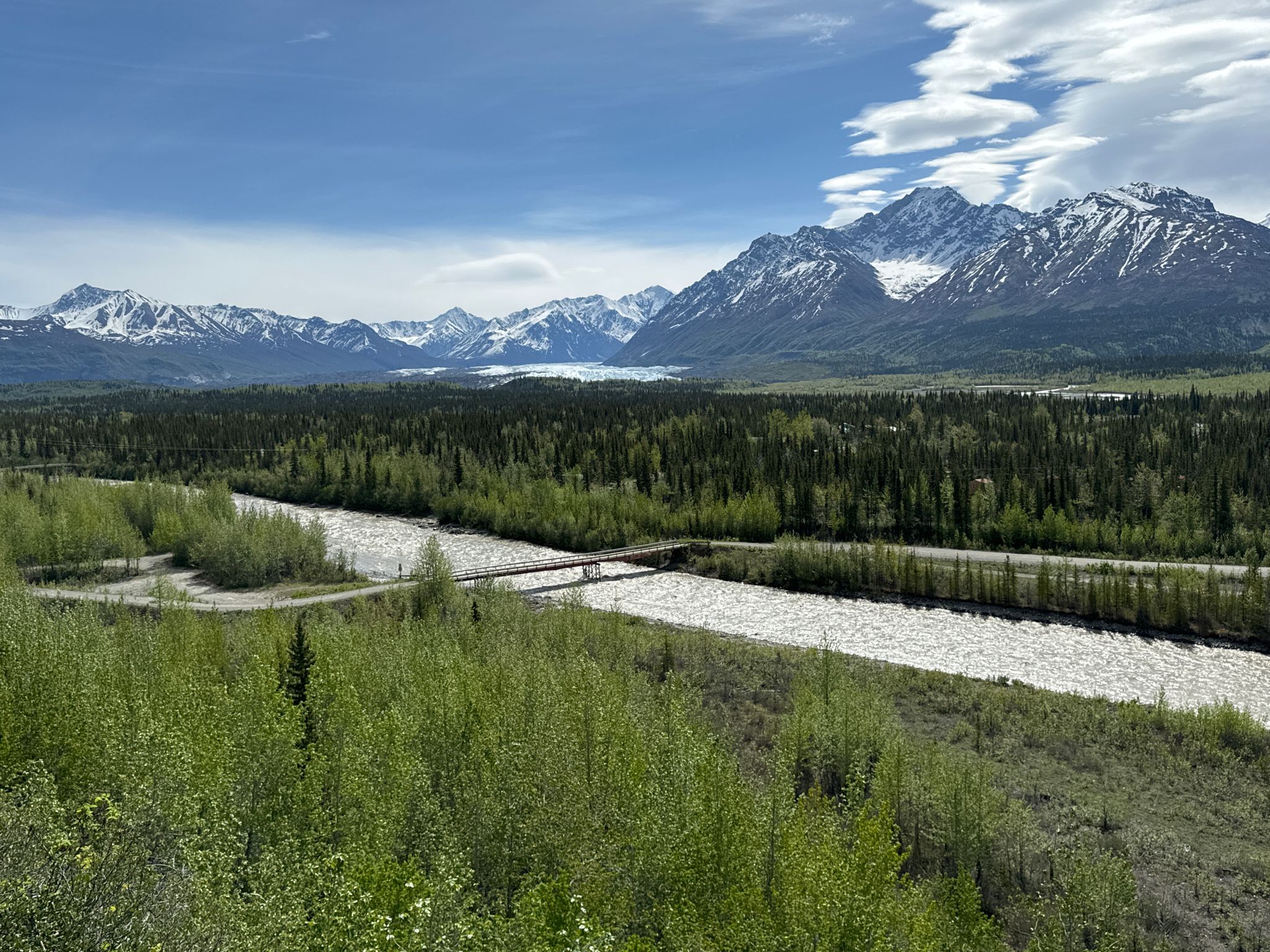 Panoramic view of a river, forest, and snow-capped mountains under a bright sky. - Edge Nature Trail