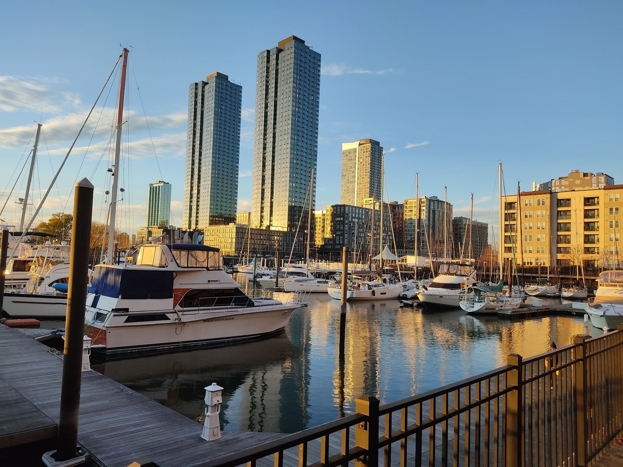 Marina with boats docked, tall buildings reflecting golden hour light. - Morris Canal Greenway