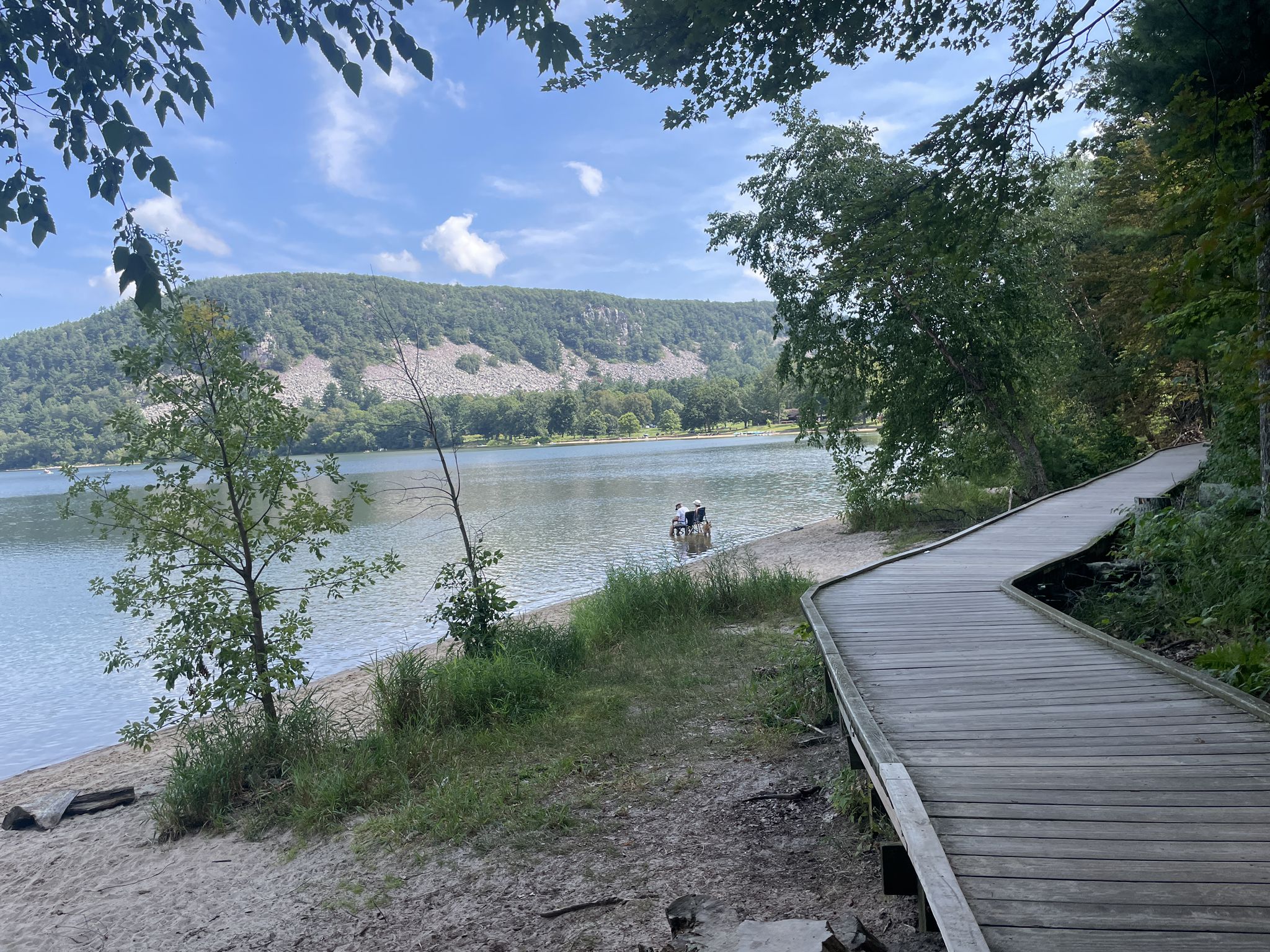 Wooden boardwalk next to a sandy lake shore with a person in the water. - Ringling Bungalow Foundation loop from Devil's Lake State Park