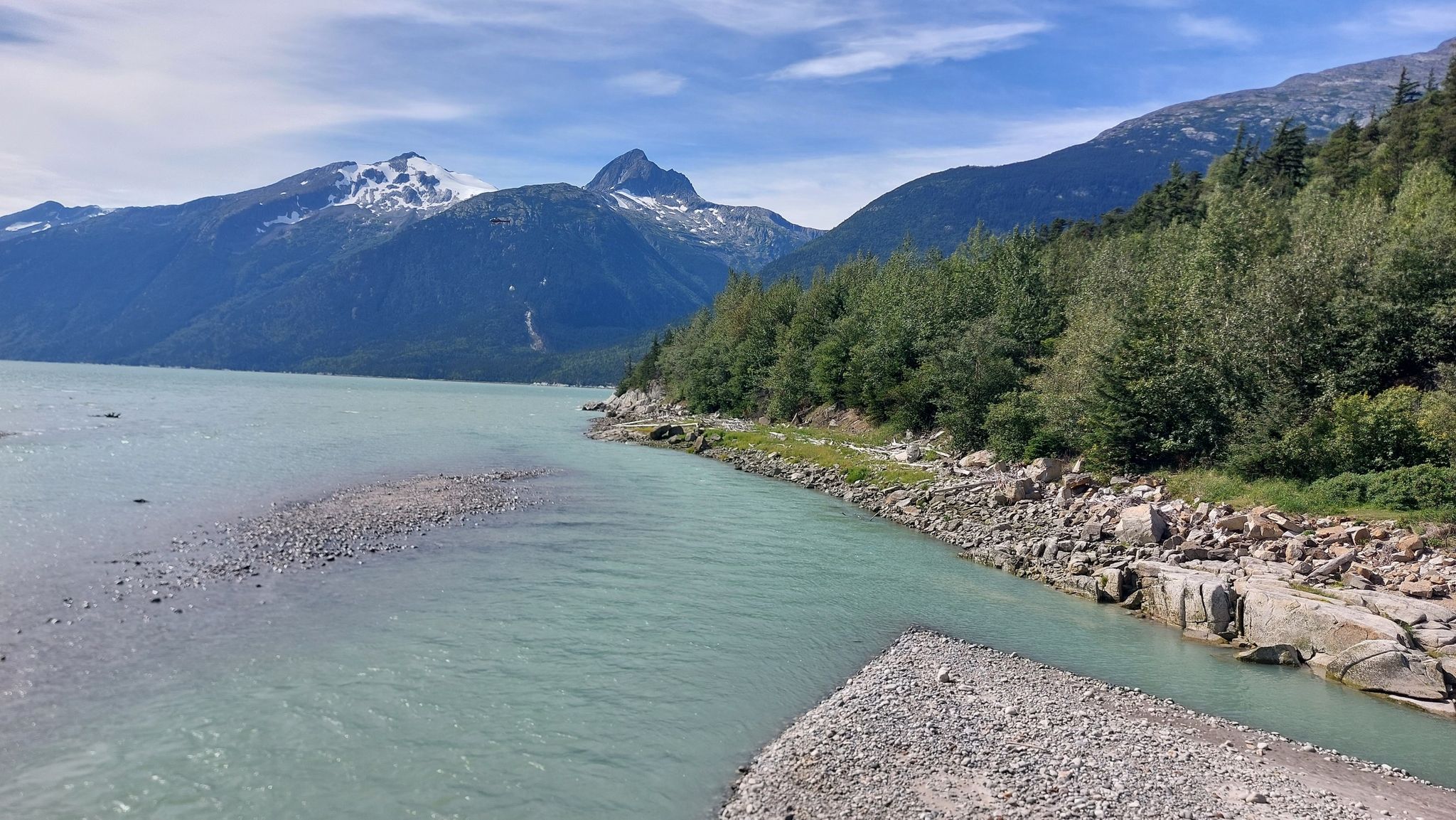 Turquoise river flows past forested hills and distant snow-capped mountains. - Yakutania Point and Smuggler's Cove Trail