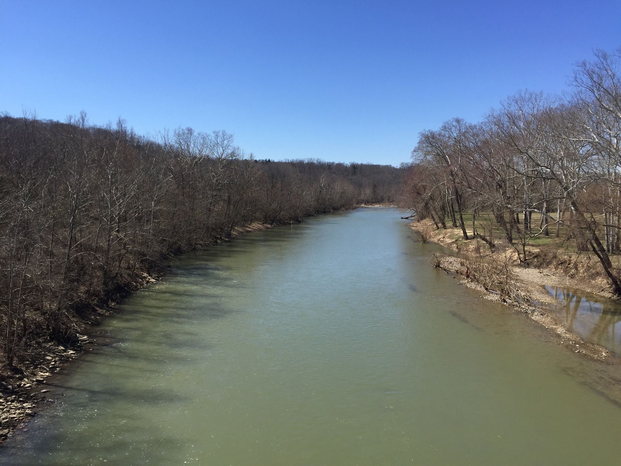 Wide river flowing between banks with bare trees under a clear blue sky. - Serpentine Wall – Kroger Hills loop from Rivertown Station