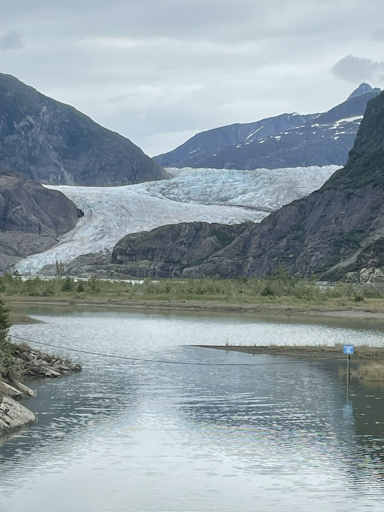 A large glacier nestled between mountains, viewed across a calm, grey lake. - Cope Park – Mendenhall Glacier Viewpoint loop from Juneau