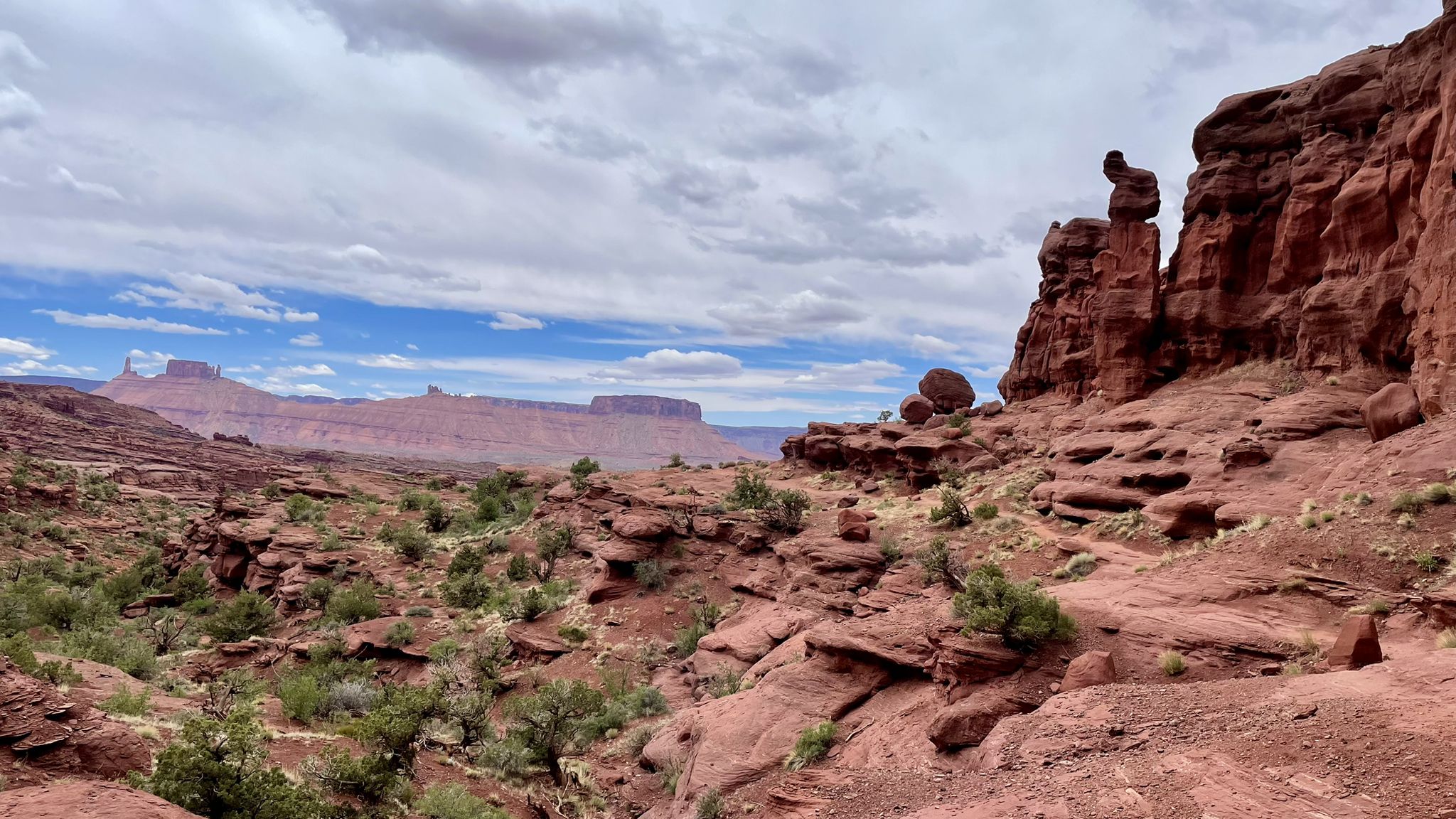 Rocky desert landscape with scattered green shrubs and distant red rock mesas. - Fisher Towers Trailhead loop from Fisher Towers Trailhead