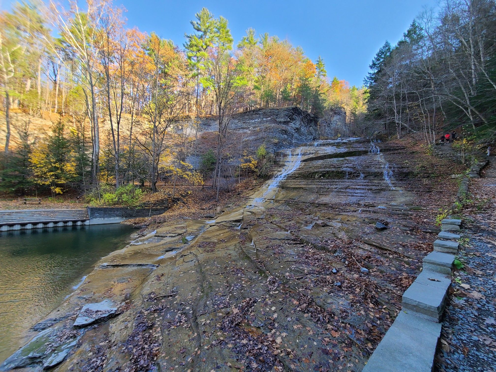 Waterfall cascades over layered rocks into a pool, surrounded by autumn trees. - Buttermilk Falls – Buttermilk Falls Overlook loop from Ithaca