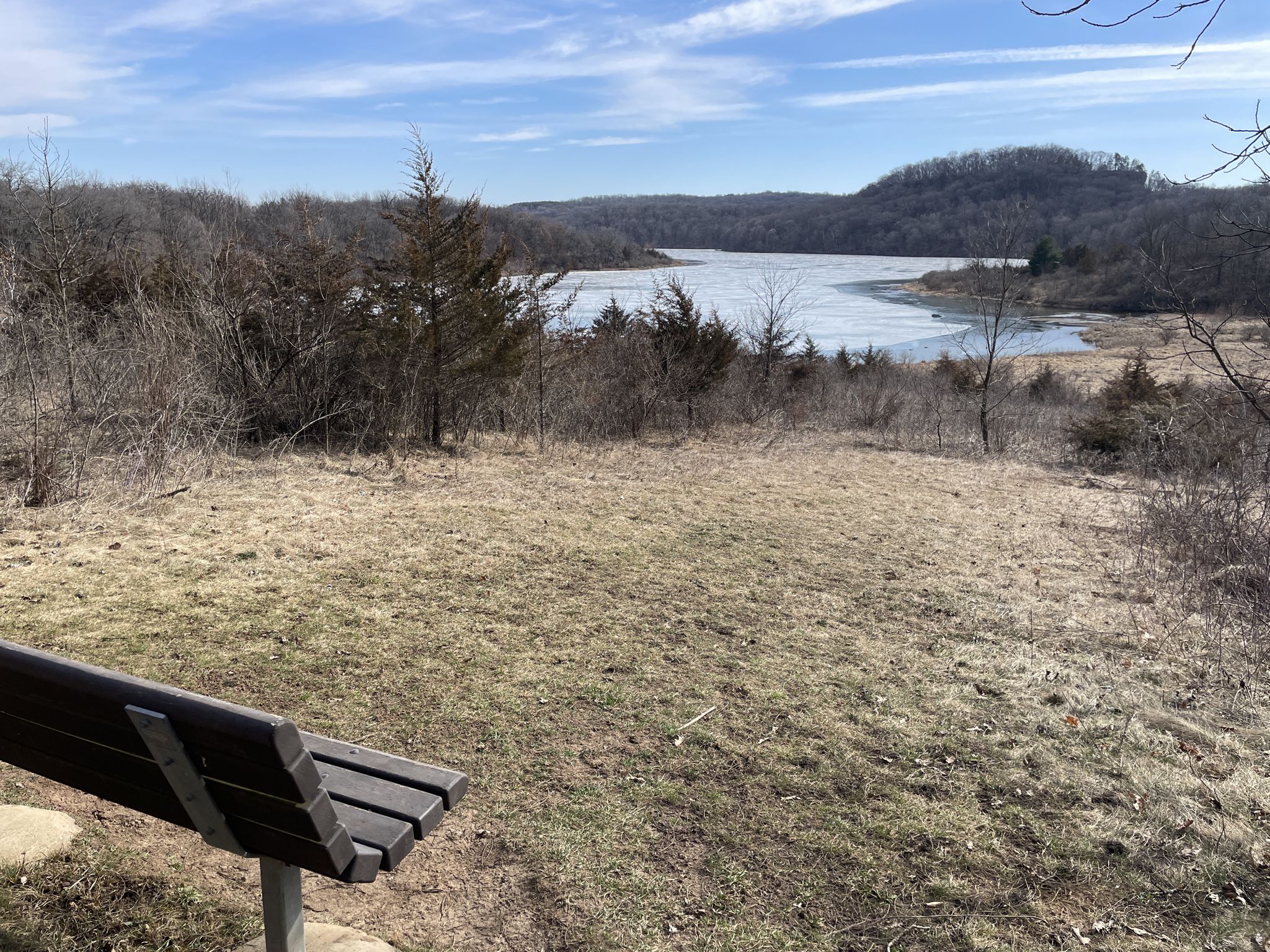 A wooden bench on a dry grassy hill overlooks a lake and distant hills. - Bunker Hill loop from Governor Dodge State Park