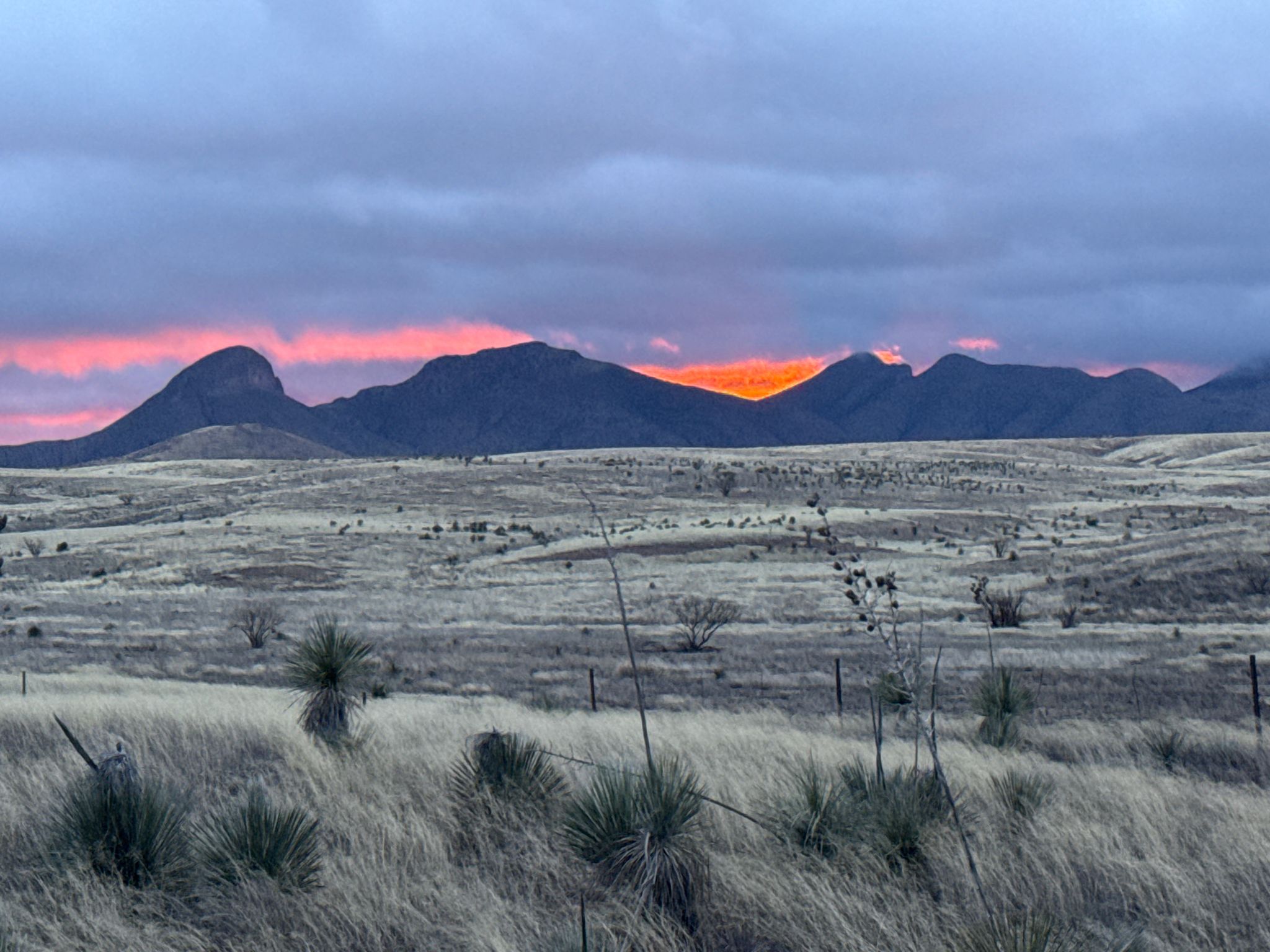 Dramatic sunset with orange glow behind dark mountains over a dry, grassy landscape. - Full Sonotia-Elgin Wine Loop