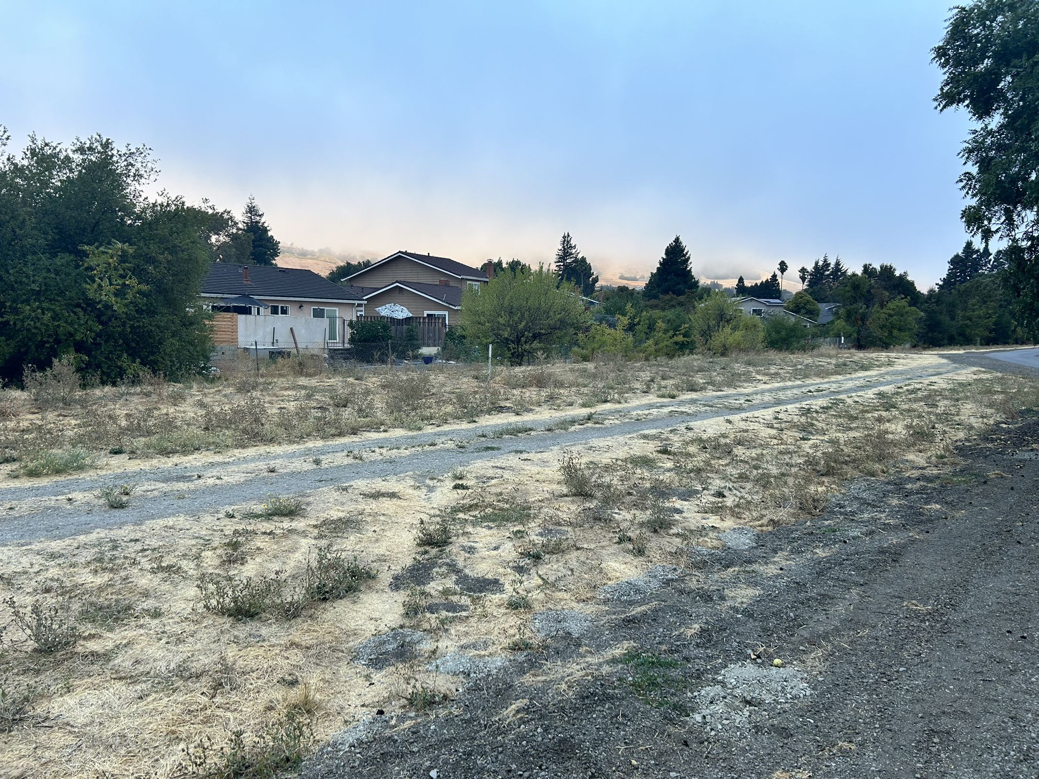 Wide dirt path through a dry field with houses under an overcast sky. - Iron Horse Trail – San Ramon iron horse trail loop from Danville