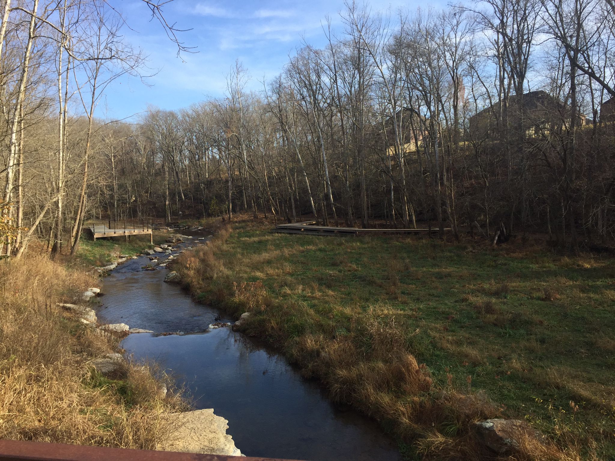 A winding river flows past grassy banks and bare trees on a sunny day. - Appleblossom Trail
