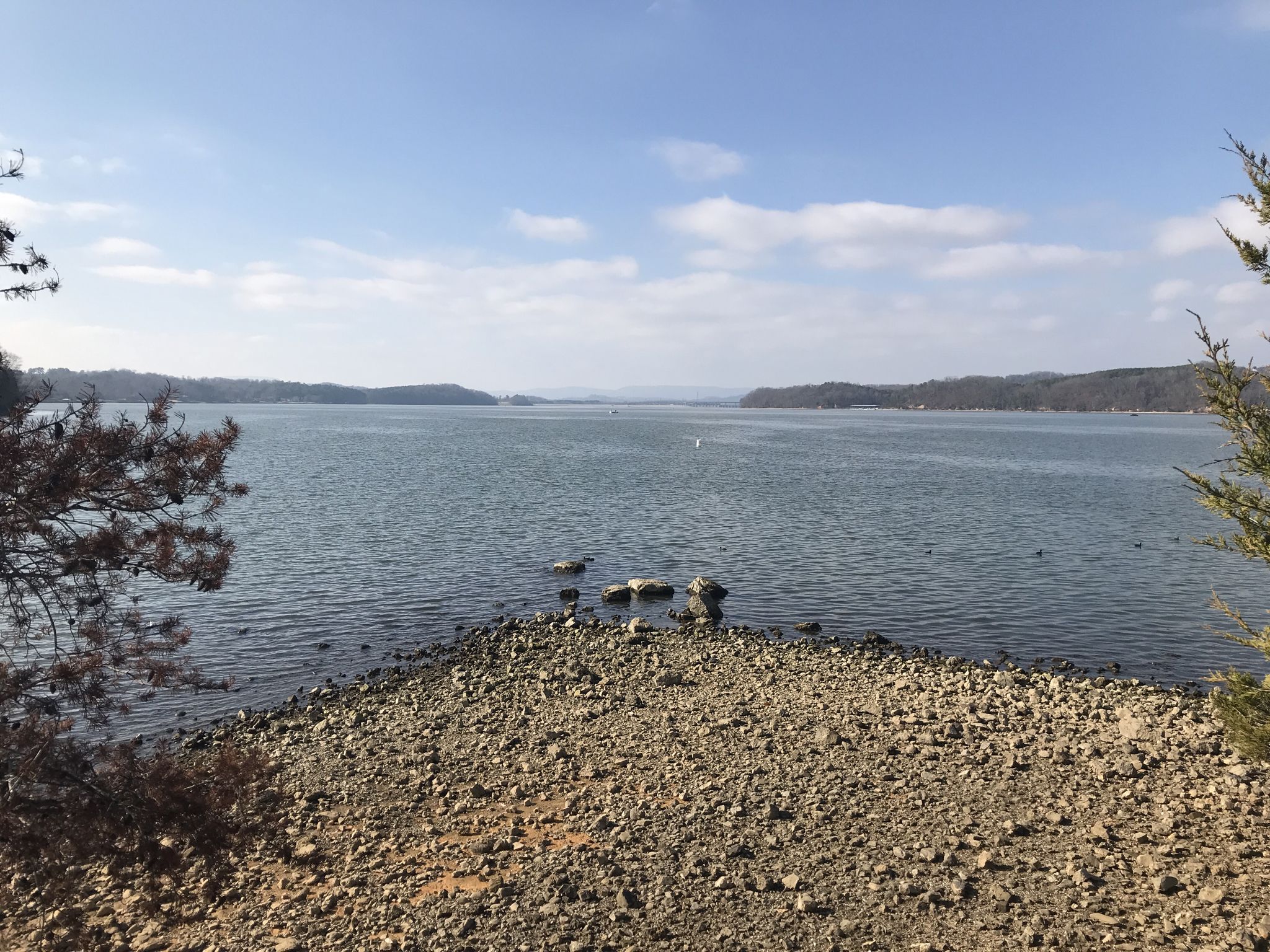 Wide lake with rocky shore under a bright, clear sky. - Outer Loop Trail