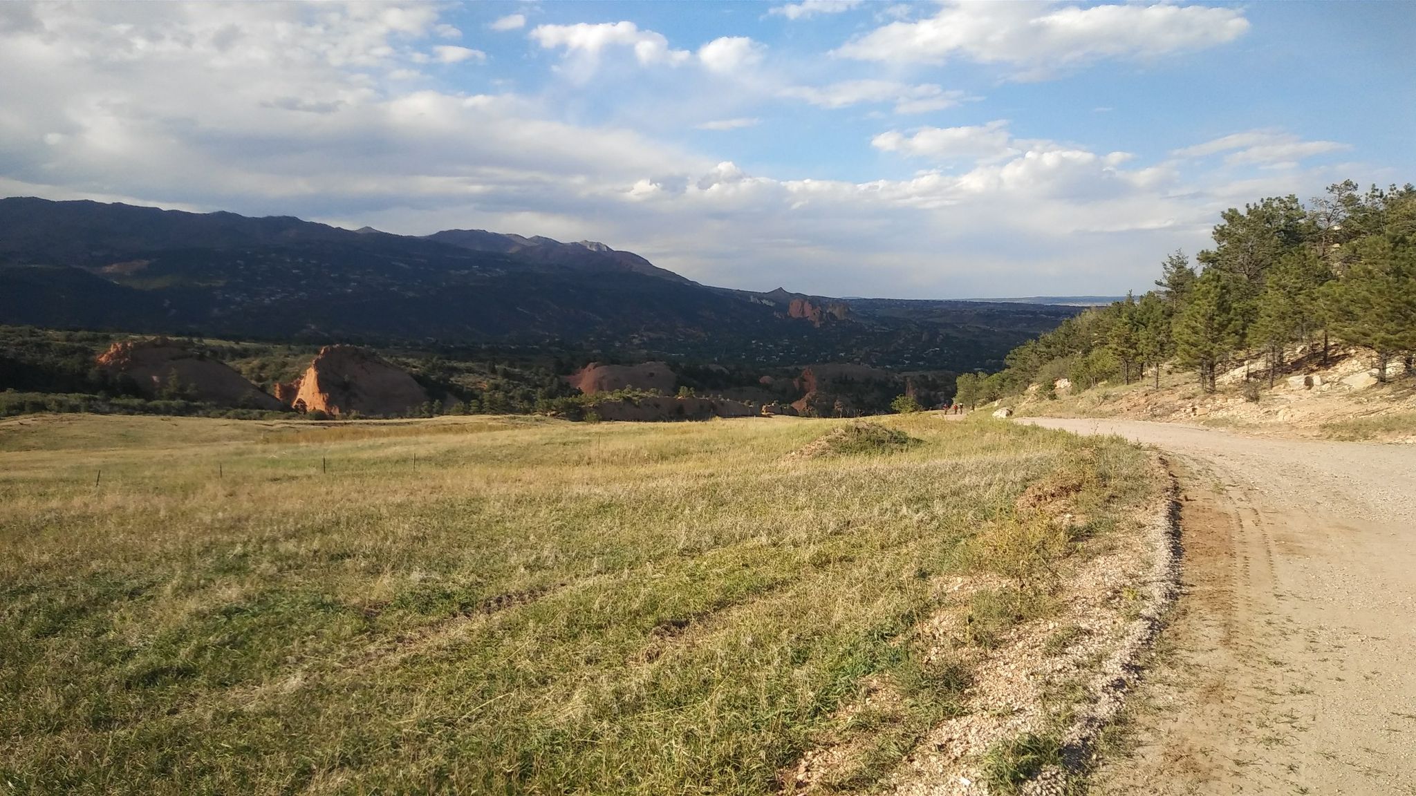 Wide grassy field next to a dirt road, with distant red rock formations. - Pikes Peak Greenway – Popsicle Bridge loop from Colorado Springs