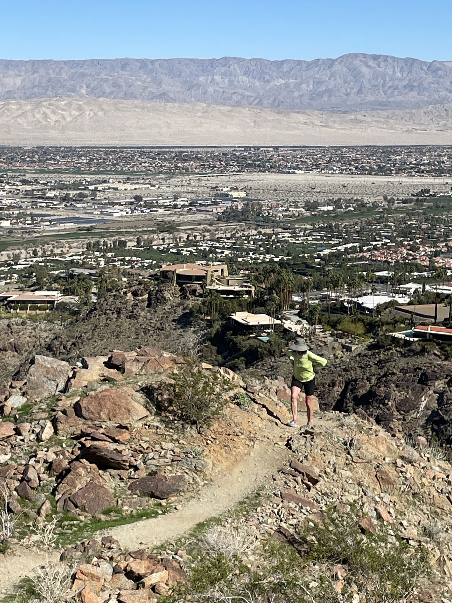 A person hikes a rocky desert trail overlooking a city and mountains. - Garstin, Shannon and Henderson Trail Loop