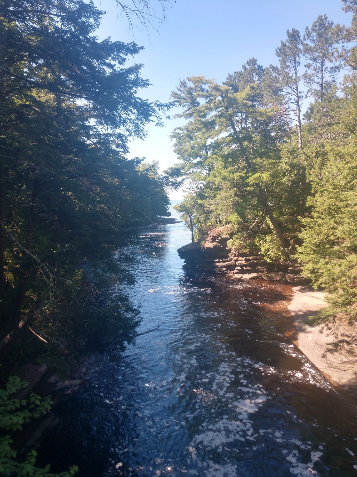 River flows through a narrow, tree-lined gorge under a clear blue sky. - Lake Superior Trail