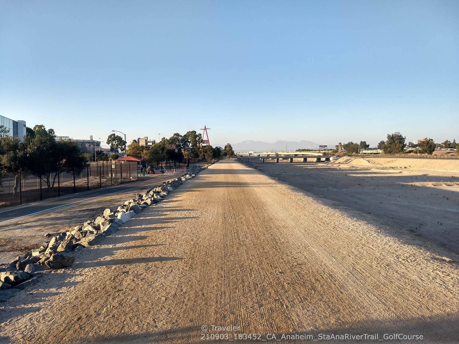 Wide, flat dirt path with distant bridges and mountains under clear sky. - Angel Stadium – Talbert Regional Park loop from Valley High School