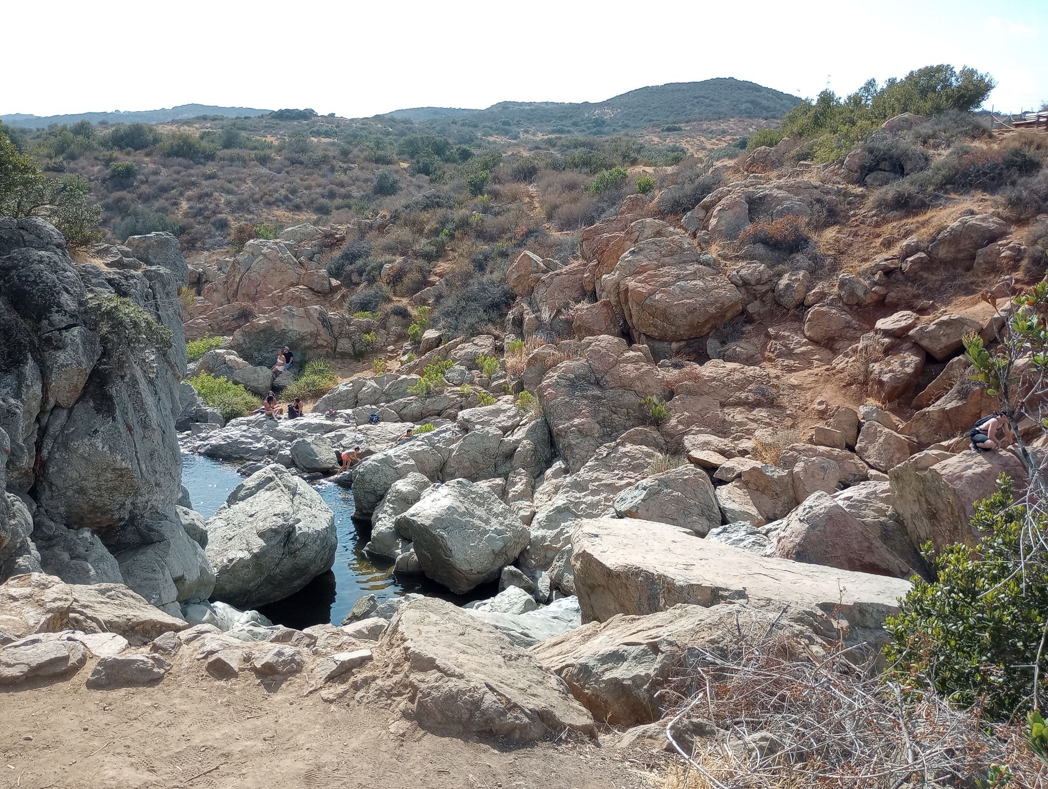 A rocky canyon with small pools and distant people among boulders. Bright daylight. - Los Peñasquitos Waterfall – Los Peñasquitos Falls loop from Del Mar Mesa Preserve