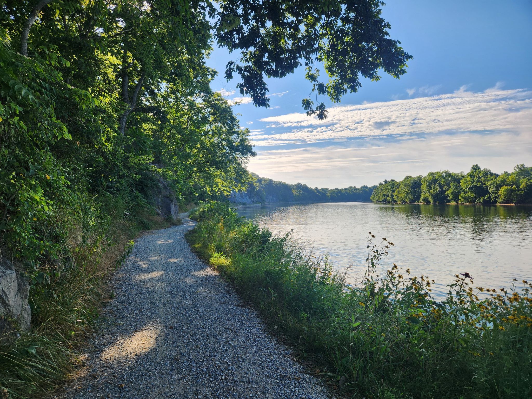 Gravel path next to a wide river, green trees, bright sunny day. - Big Slackwater View – Conococheague Aqueduct loop from Cedar Grove